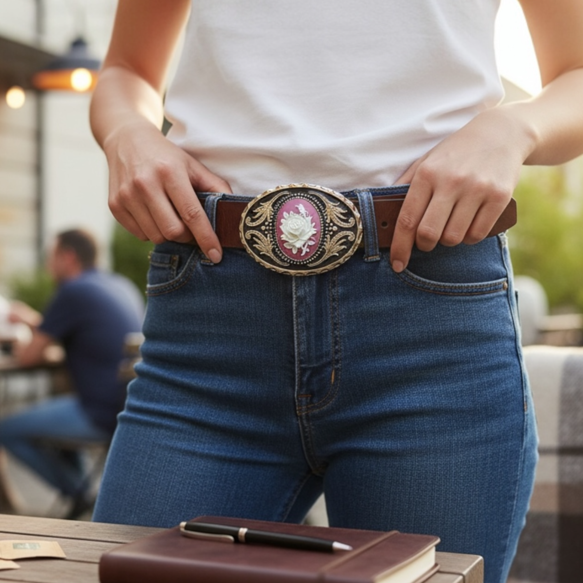 Person wearing blue jeans with a decorative silver cowgirl belt buckle with a rose, standing outdoors.
