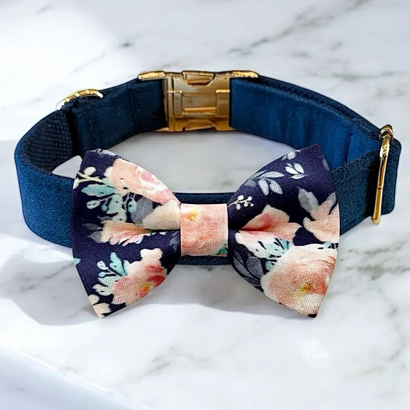 Navy blue velvet dog collar with a floral bow tie on a marble surface