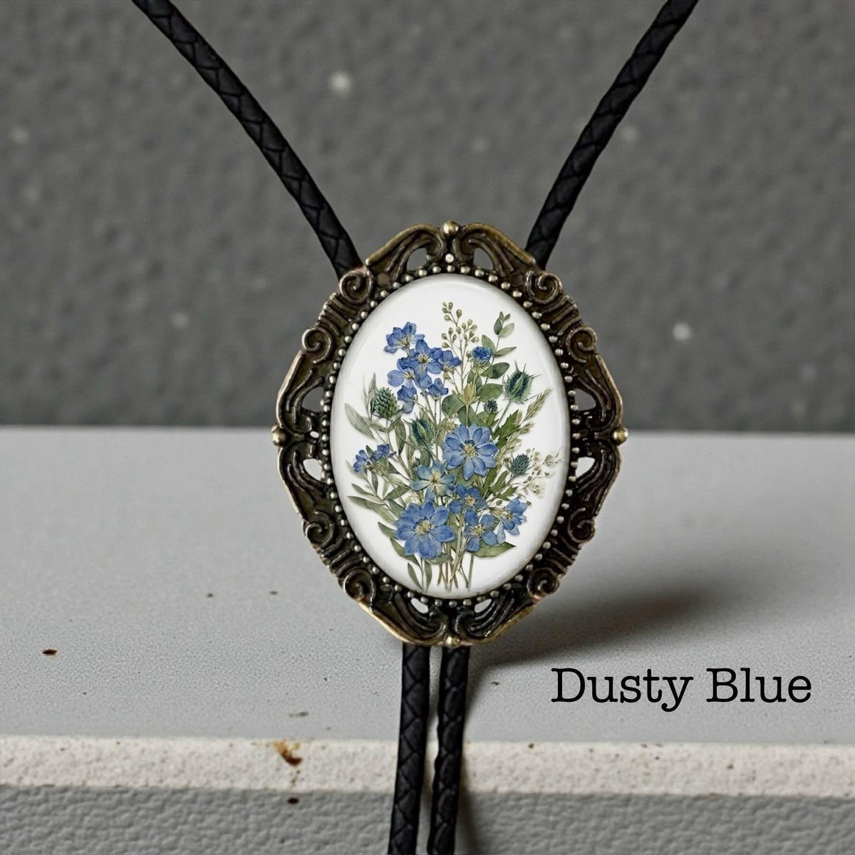 Dusty Blue floral bolo tie with bronze vintage frame and braided leather cord for groom and groomsmen rustic wedding attire.