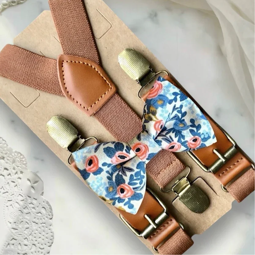 White floral bow tie with blue and pink flowers paired with cognac brown leather suspenders on kraft backing