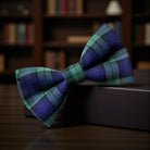 Plaid bow tie on a dark surface with a blurred bookshelf background