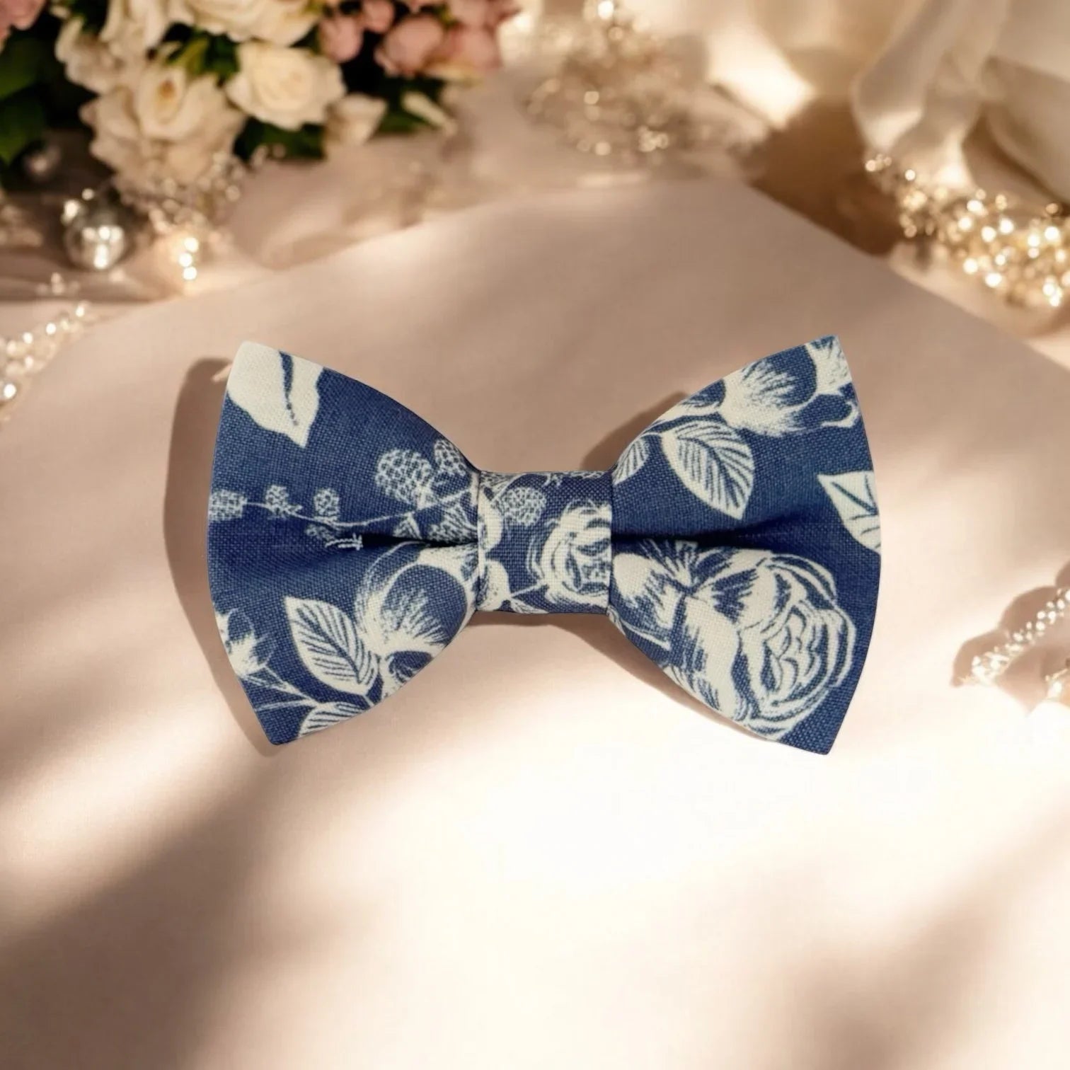 Blue floral bow tie on a white surface with blurred flowers in the background