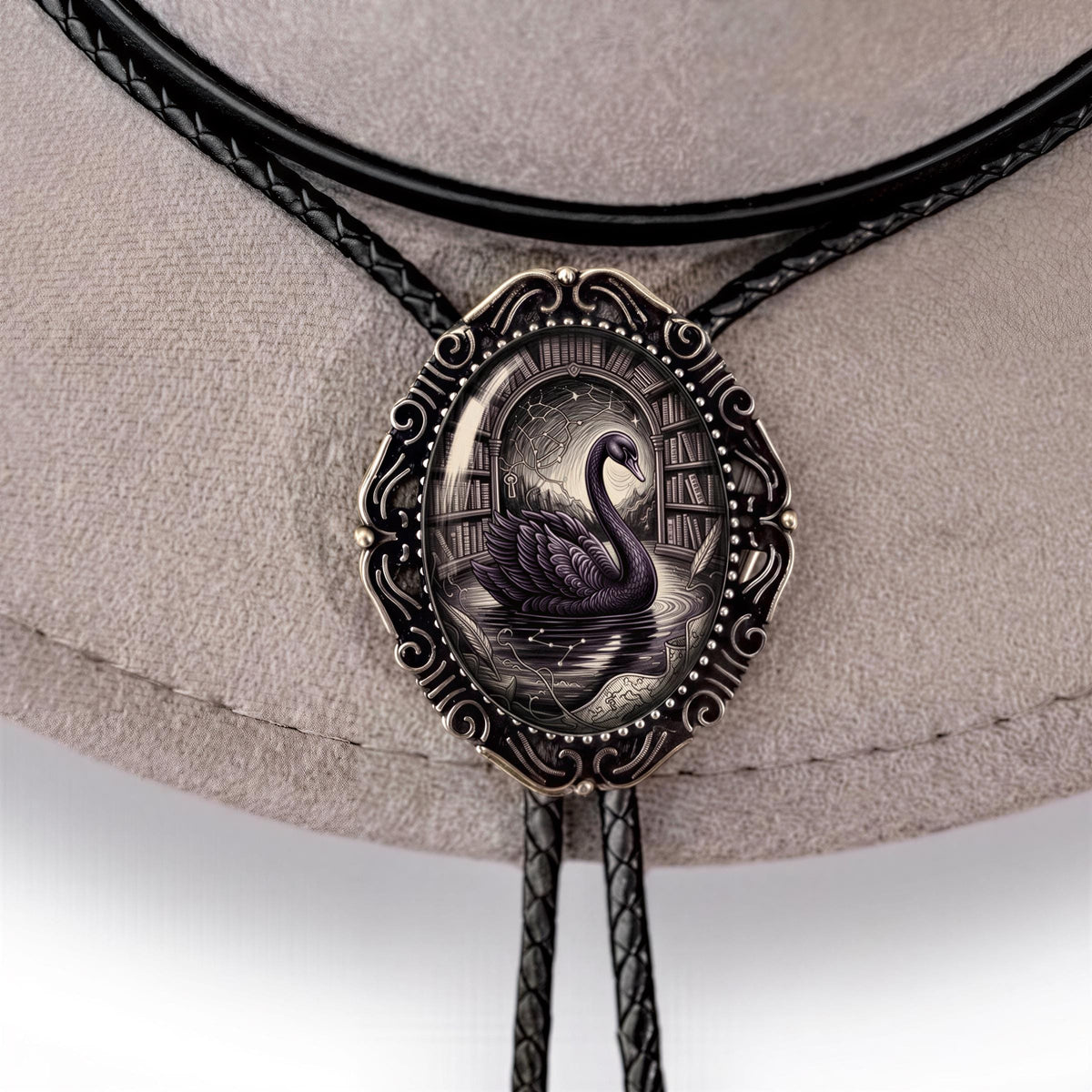 A close-up image of a decorative metal pendant featuring a black swan on a white background, with a black leather bowing cord around it.