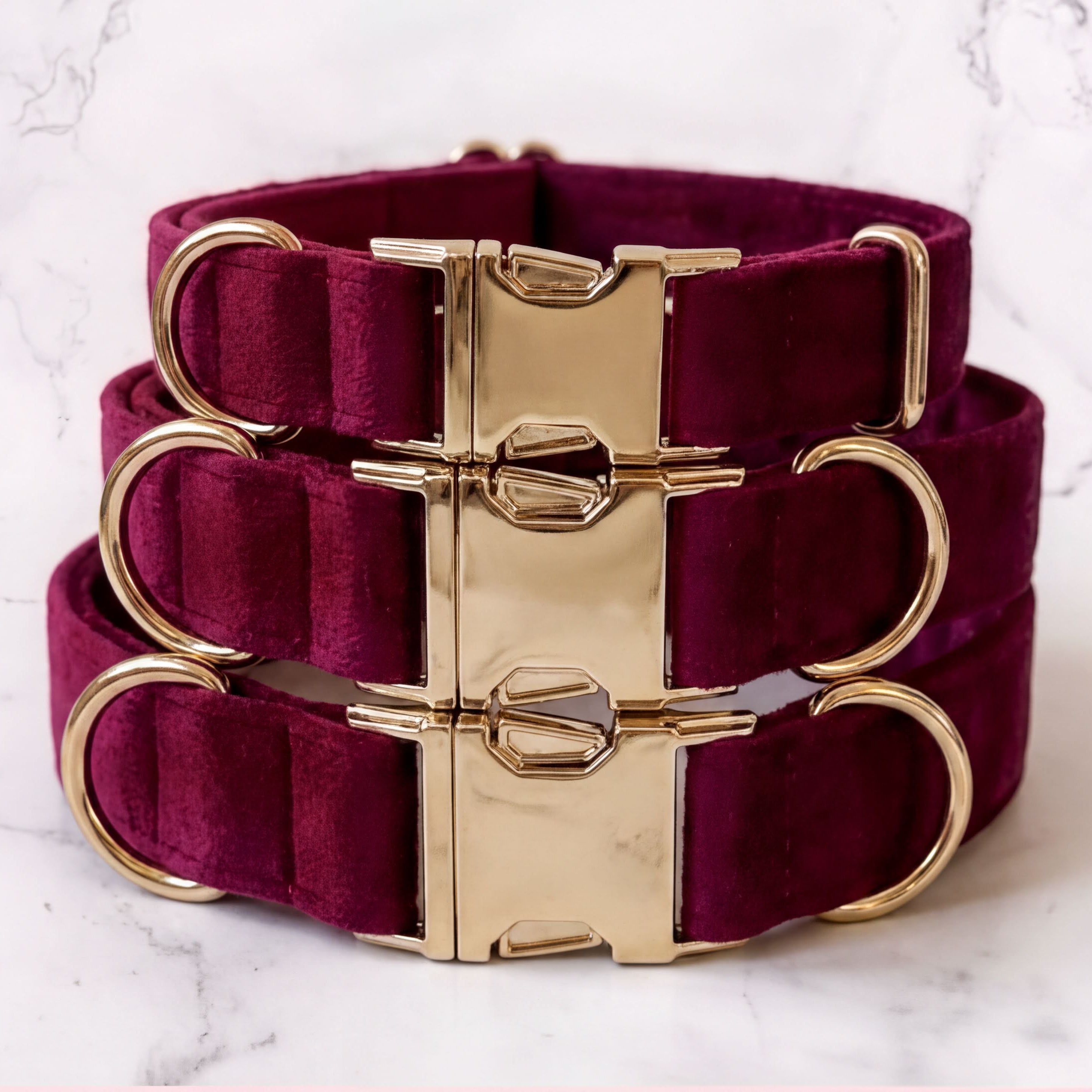 Burgundy dog collars with gold hardware on a marble background