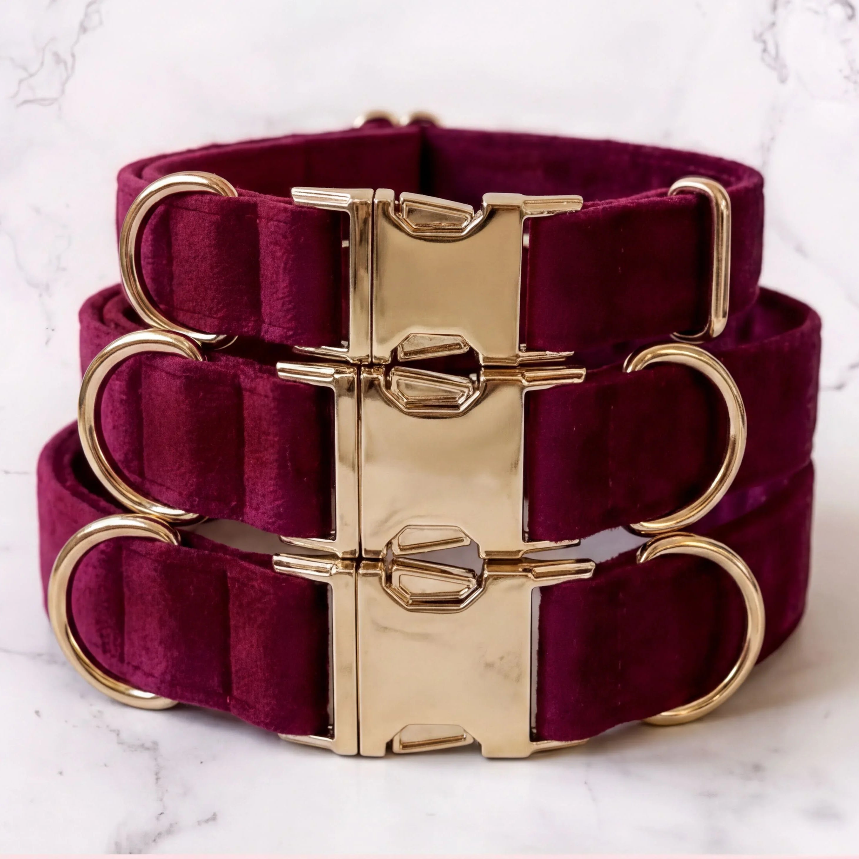 Burgundy dog collars with gold hardware on a marble background