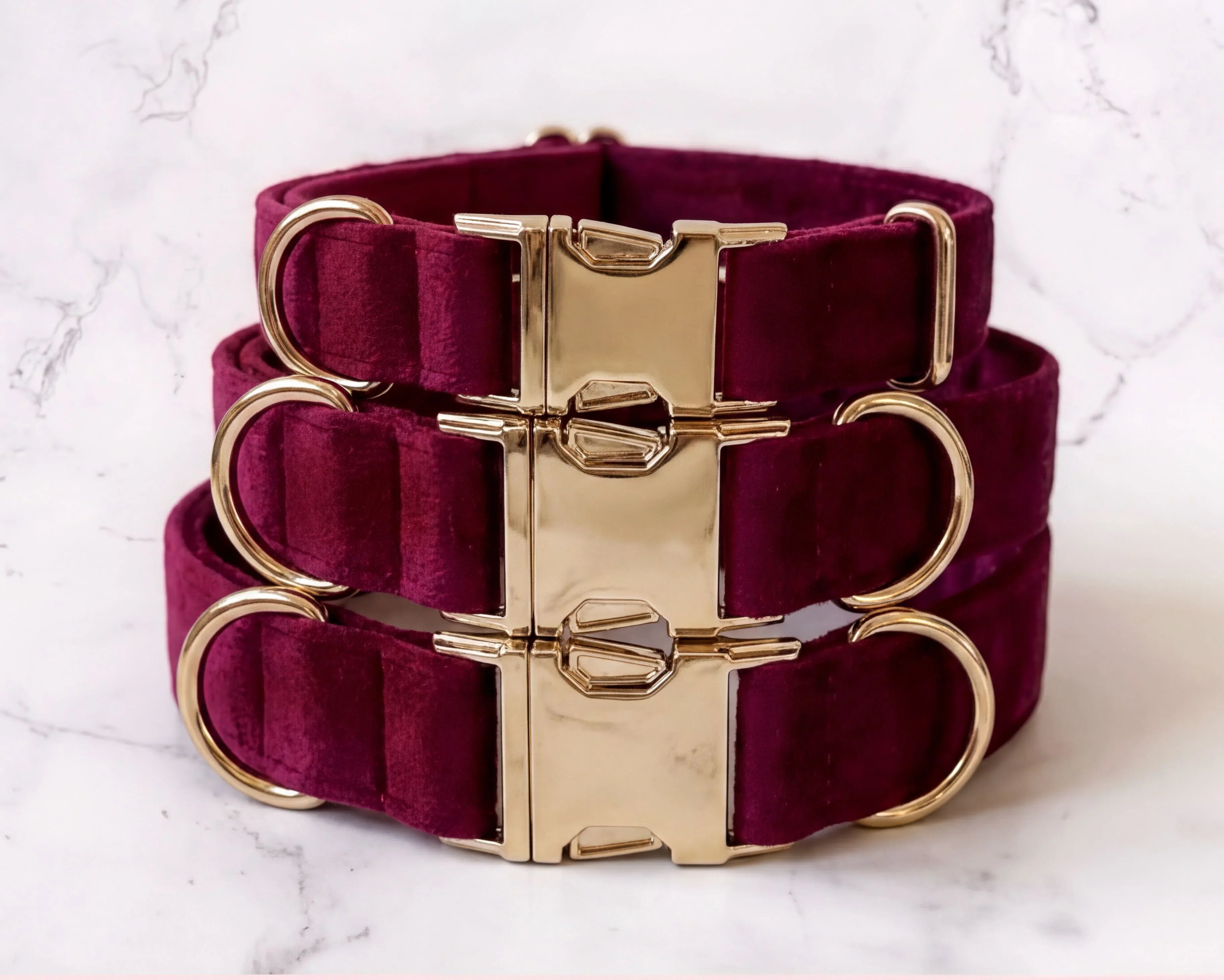 Burgundy dog collars with gold hardware on a marble background