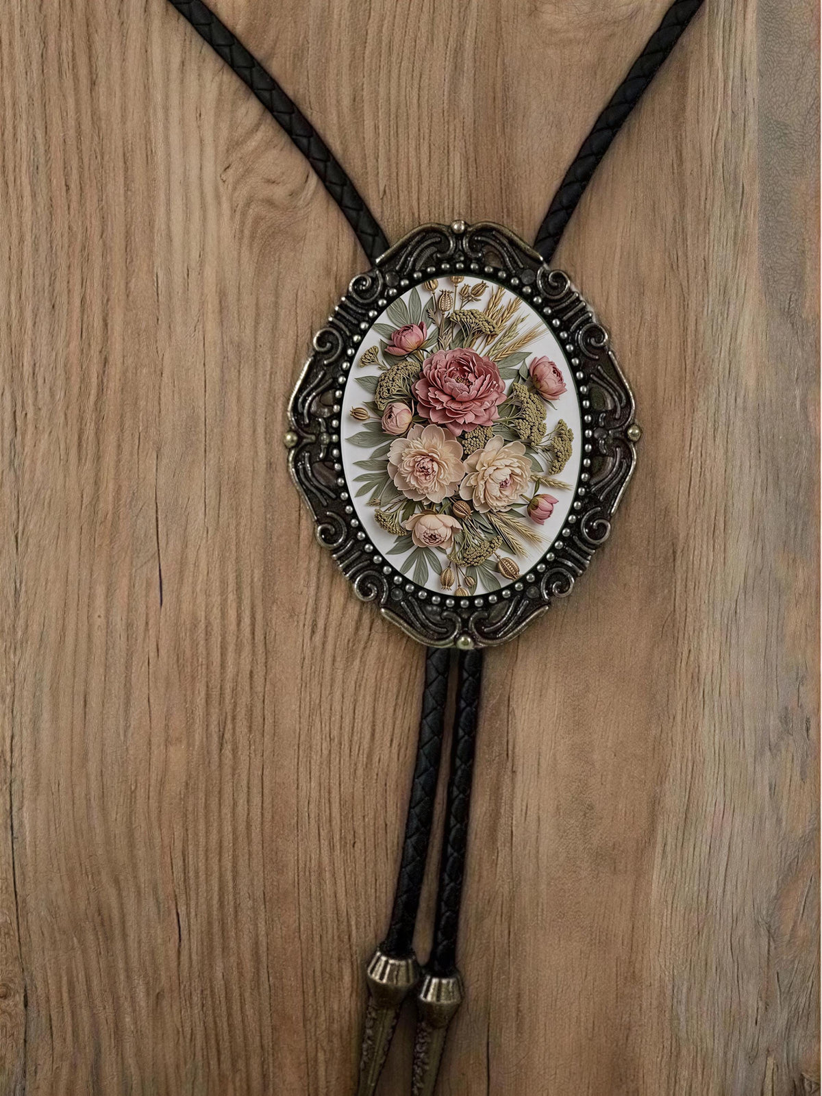A decorative floral pendant necklace with a black leather tassel hanging from it, displayed on a wooden surface.