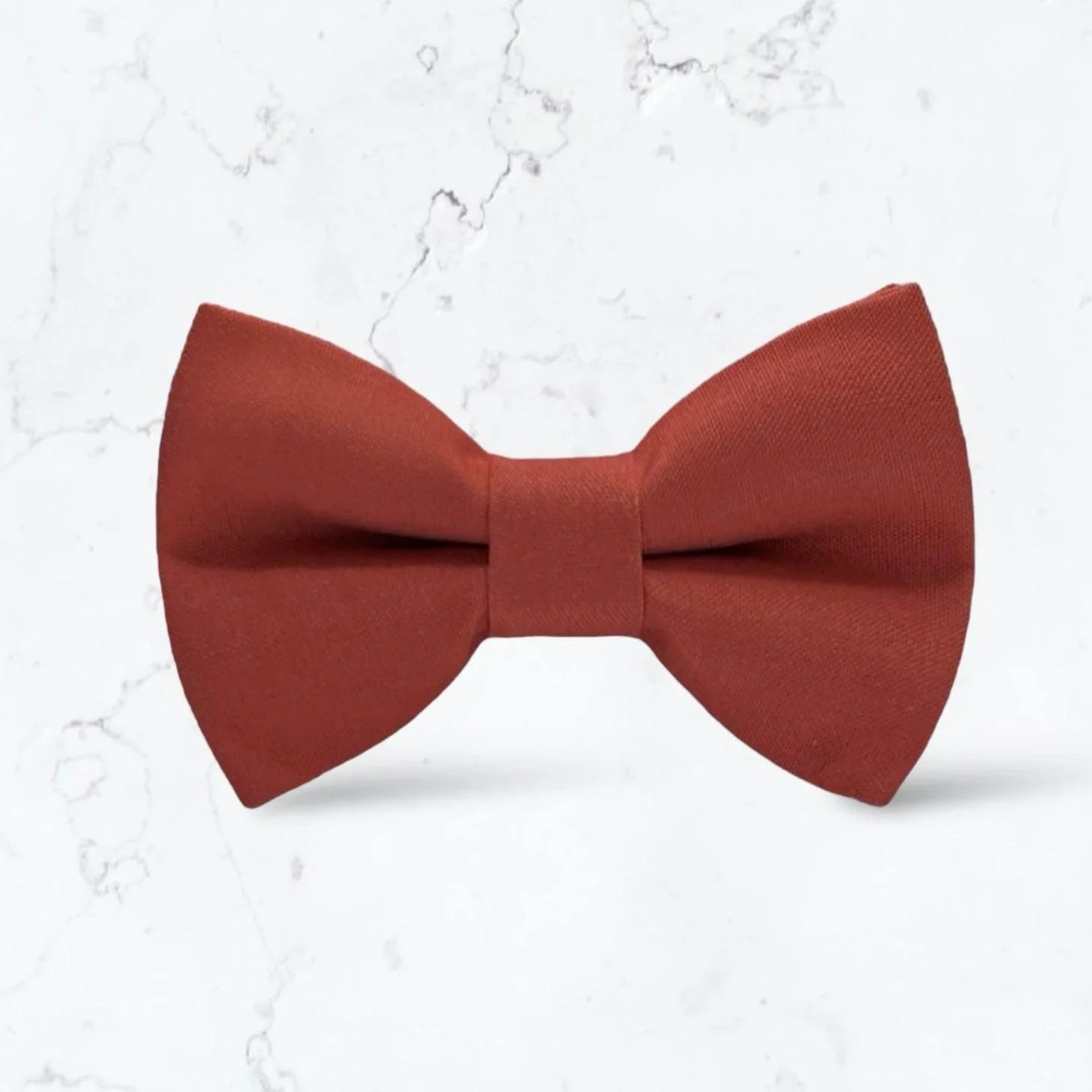 A burnt orange bow tie on a white marble background for groomsmen, men, toddlers and ring bearers.