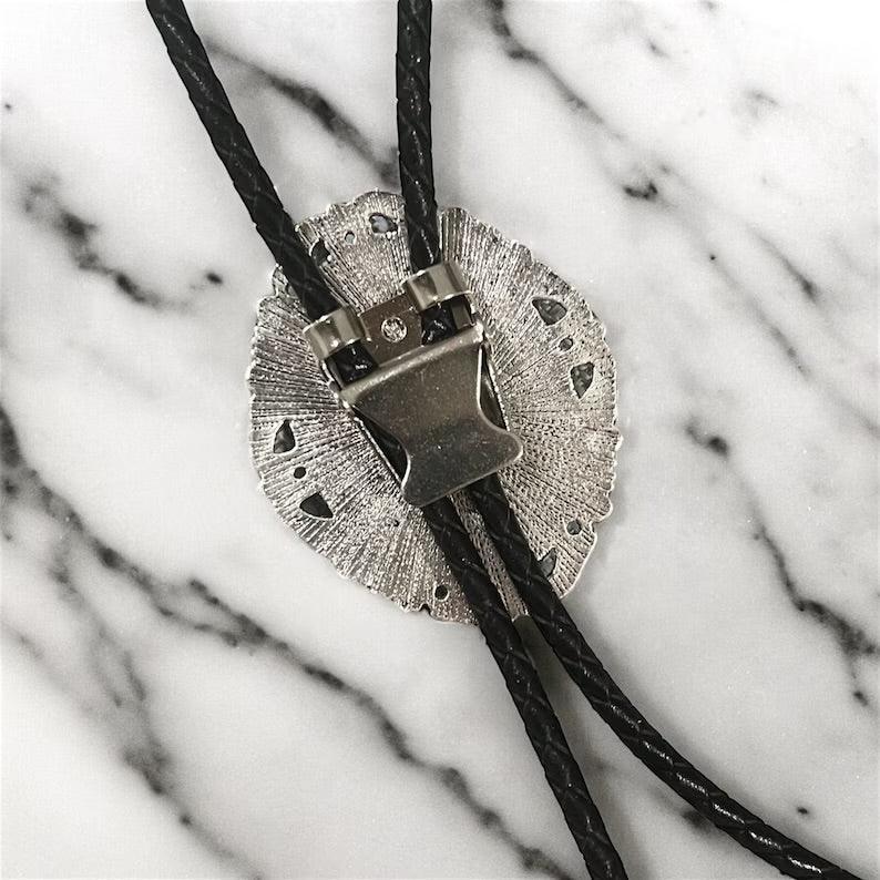 Silver tips for a bolo tie shown on black leather cord next to a green plant