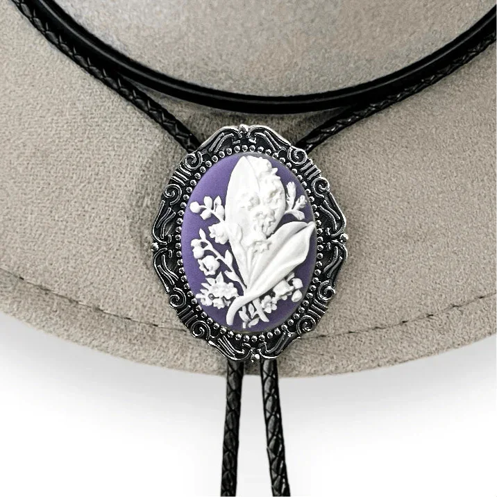 Close up of purple Lily of the Valley bolo tie cameo showing white floral relief on an ornate metal setting.