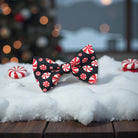 Bow tie with peppermint candy pattern on a snowy surface with blurred Christmas tree in the background