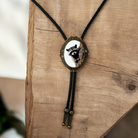 Western Bolo Tie with Raccoon with black leather cord on a wooden wall.