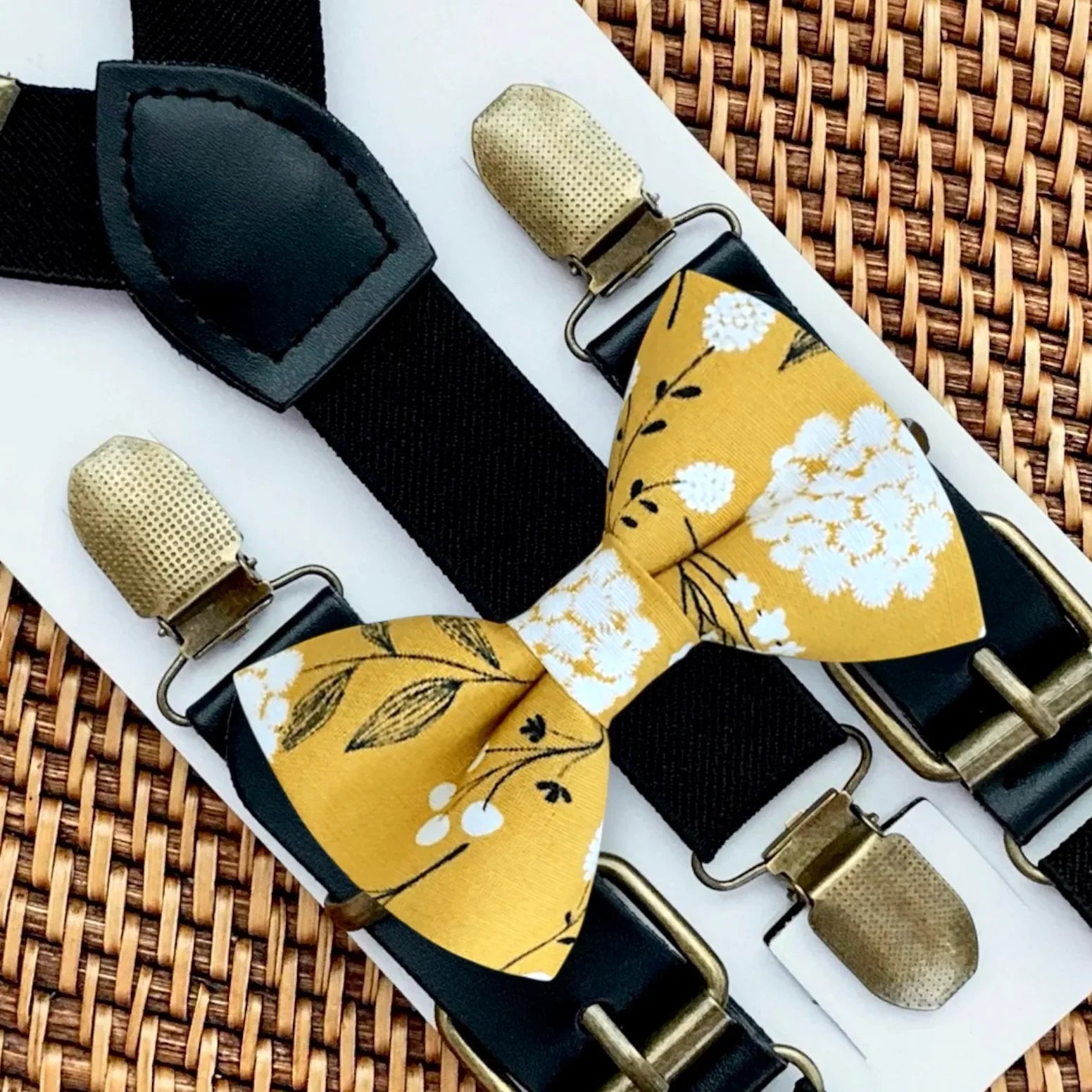 Mustard floral bow tie with white blossoms paired with black suspenders.