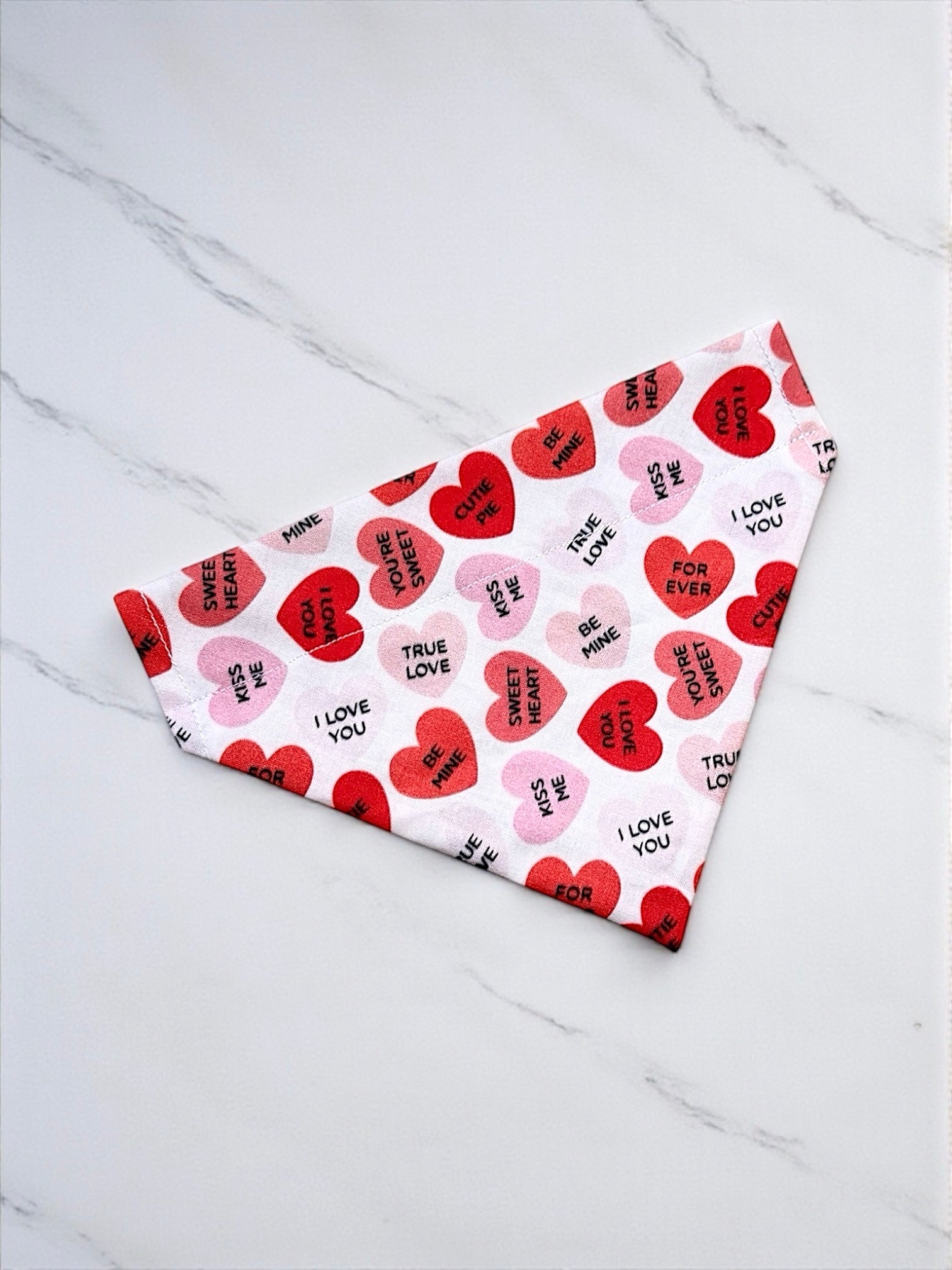 Heart-shaped dog bandana on a white tiled floor