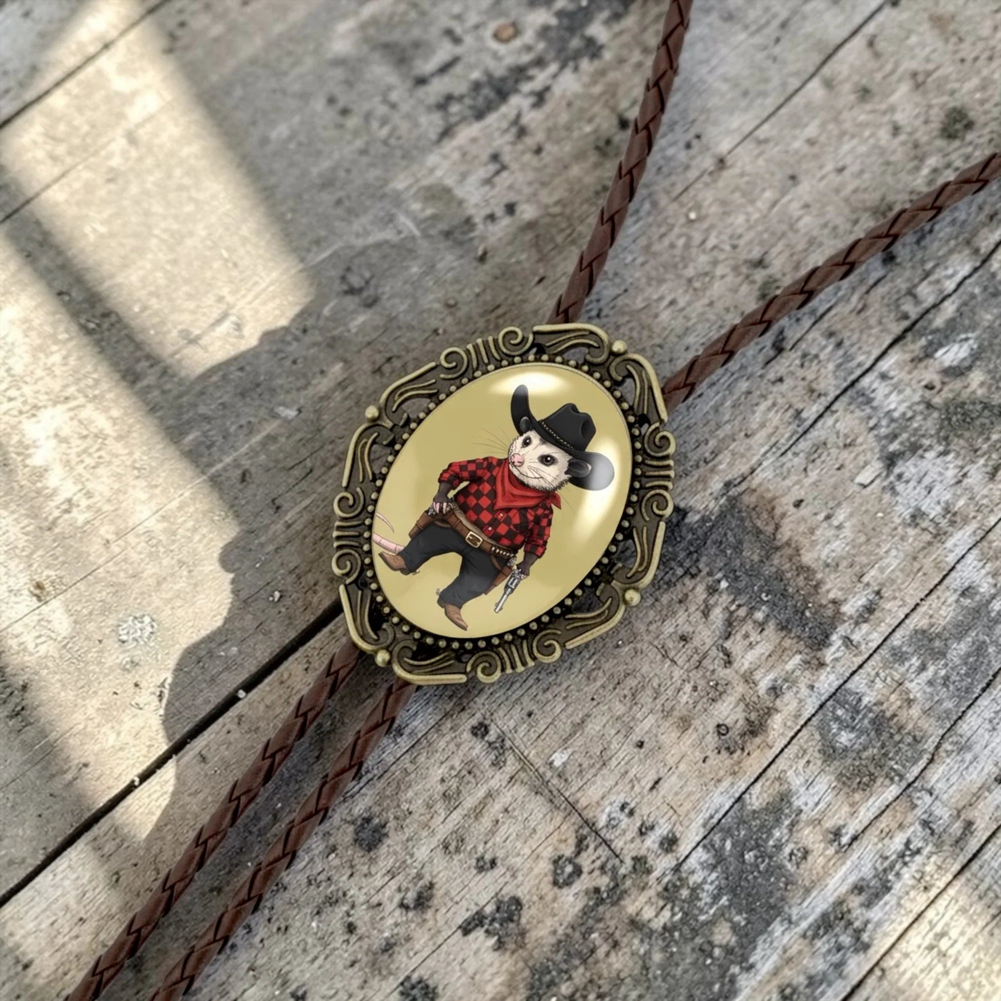 Bolo tie size chart from The Bold Bow Tie. The image displays a braided leather bolo tie with a round silver concho-style slide and silver metal tips, set against a multi-colored striped fabric background. A vertical dotted arrow on the right spans the full length of the piece, accompanied by text indicating a 39 inch cord length.