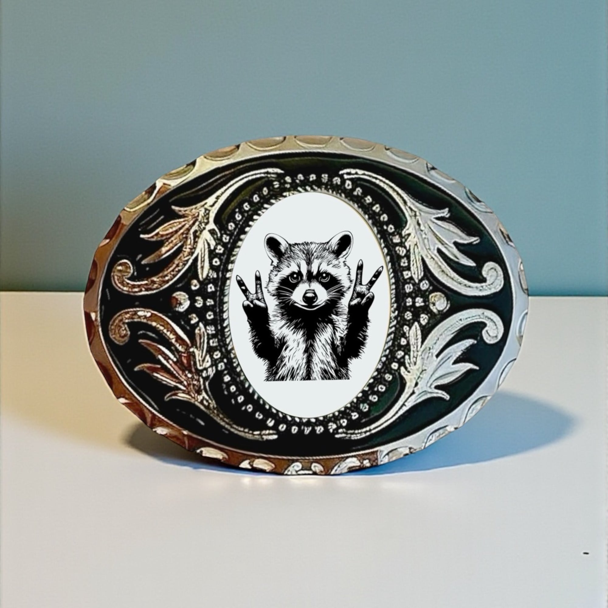 Raccoon belt buckle with a peace sign design on a white surface with a blue background.