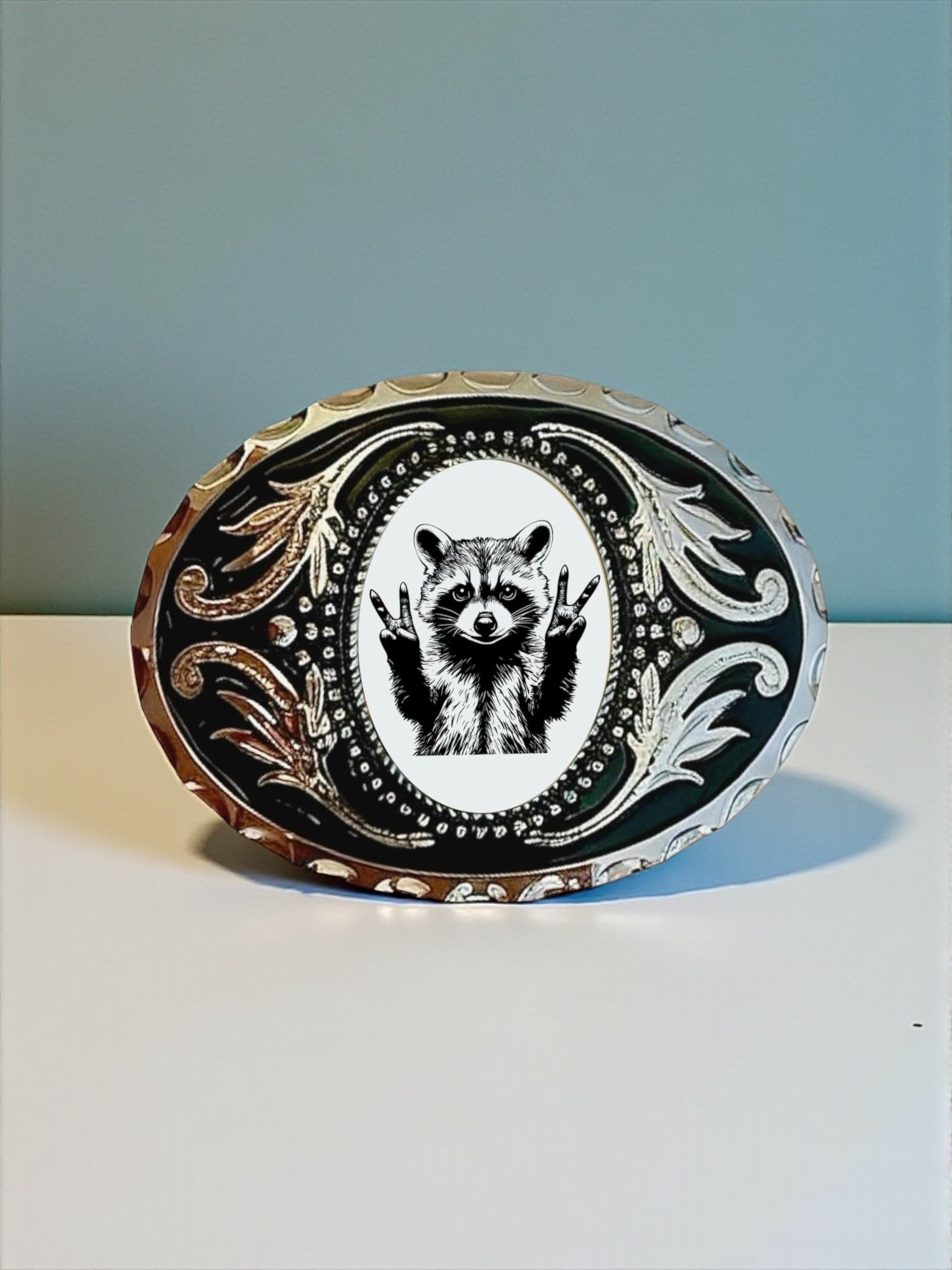 Raccoon belt buckle with a peace sign design on a white surface with a blue background.