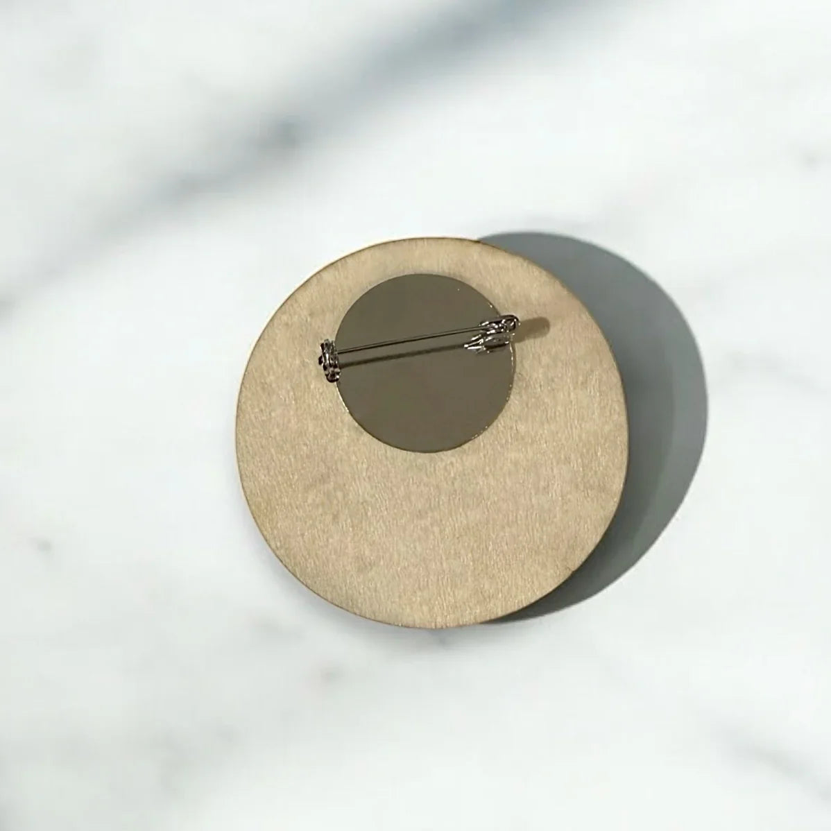 Back view of a circular wooden ring bearer badge showing the metal pin clasp.