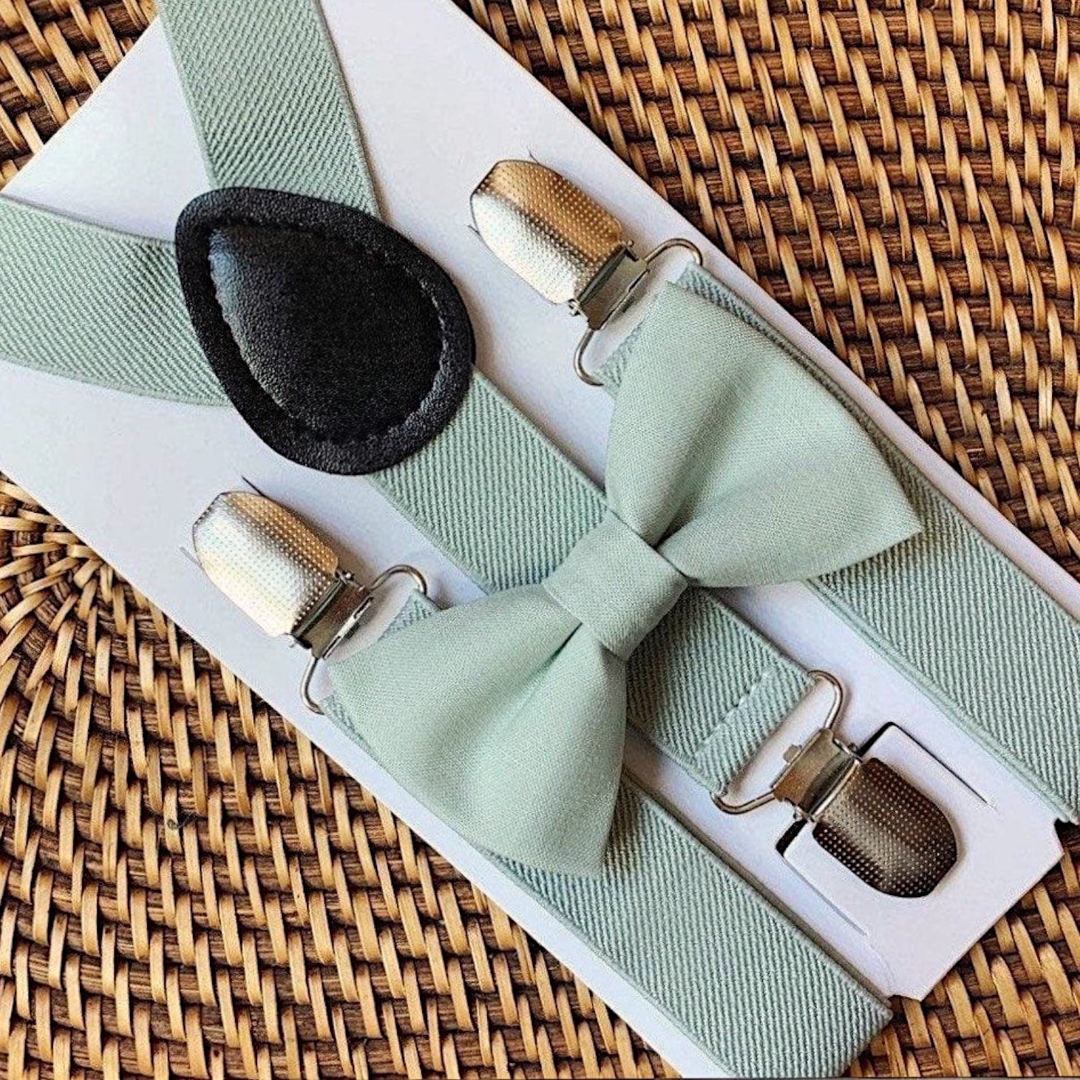 Sage green bowtie and sage green suspenders on a woven tray for a wedding by The Bold Bow Tie.