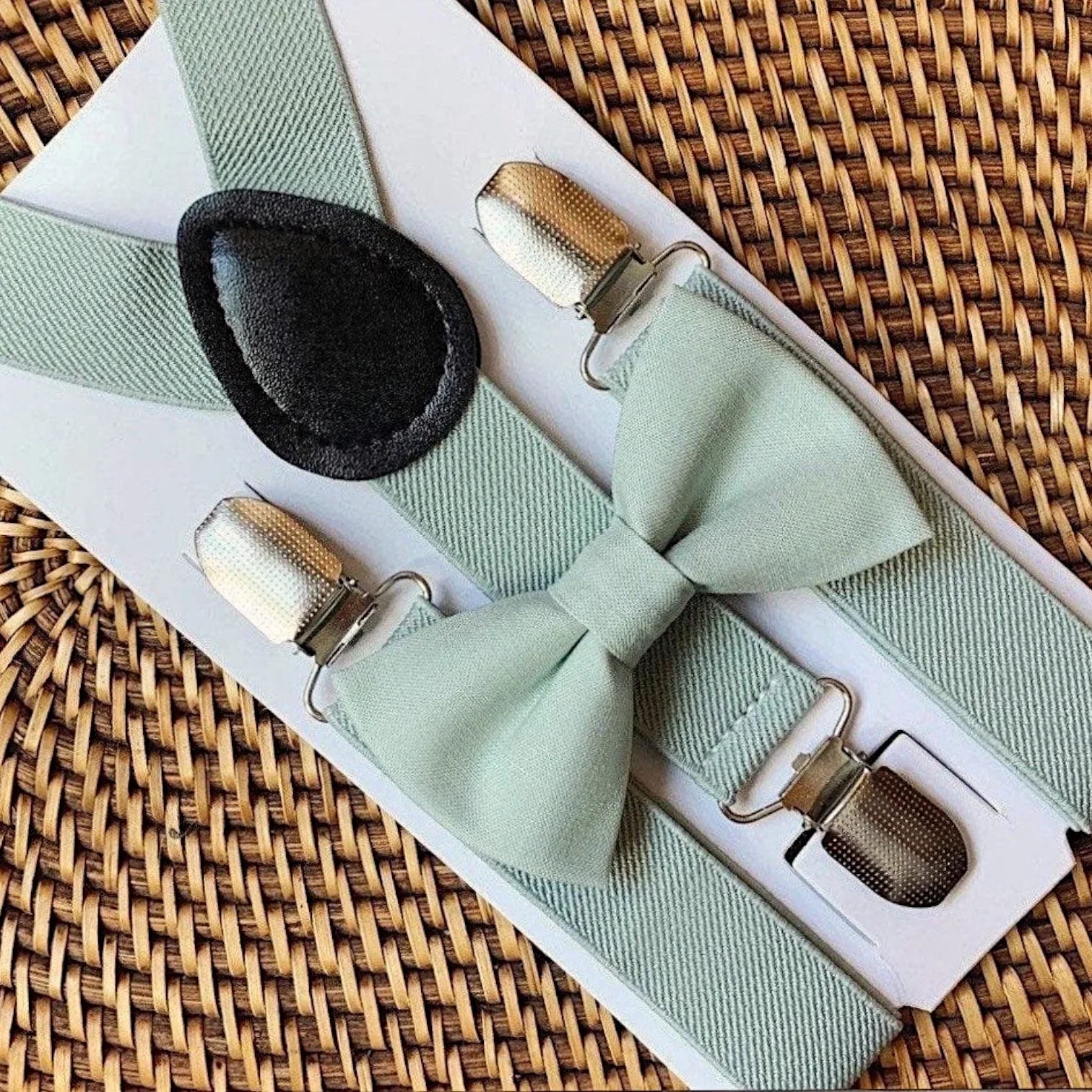 Sage green bowtie and sage green suspenders on a woven tray for a wedding by The Bold Bow Tie.