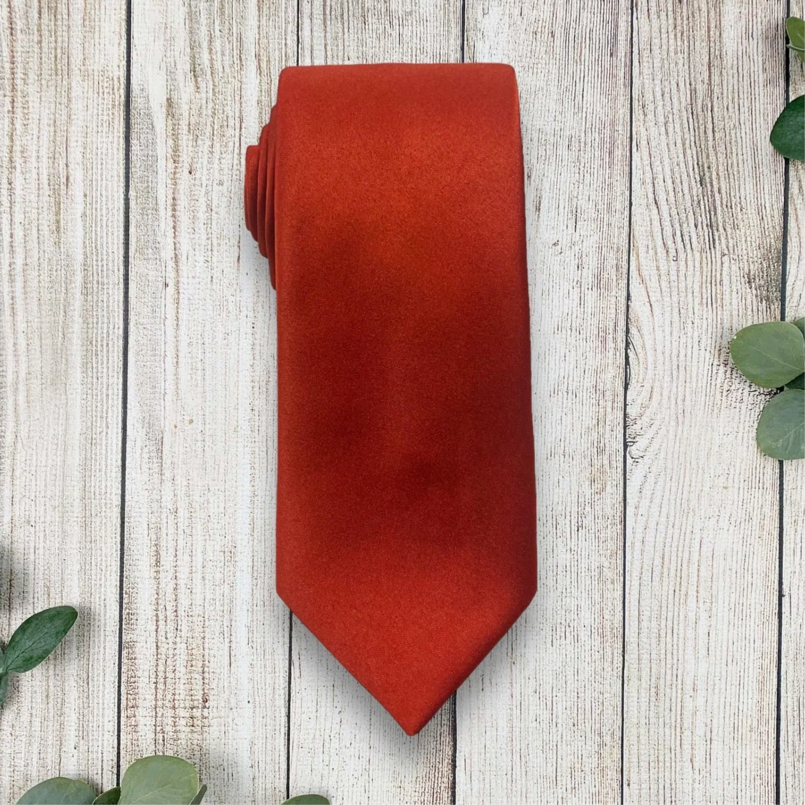 Rolled burnt orange satin necktie on light wood planks