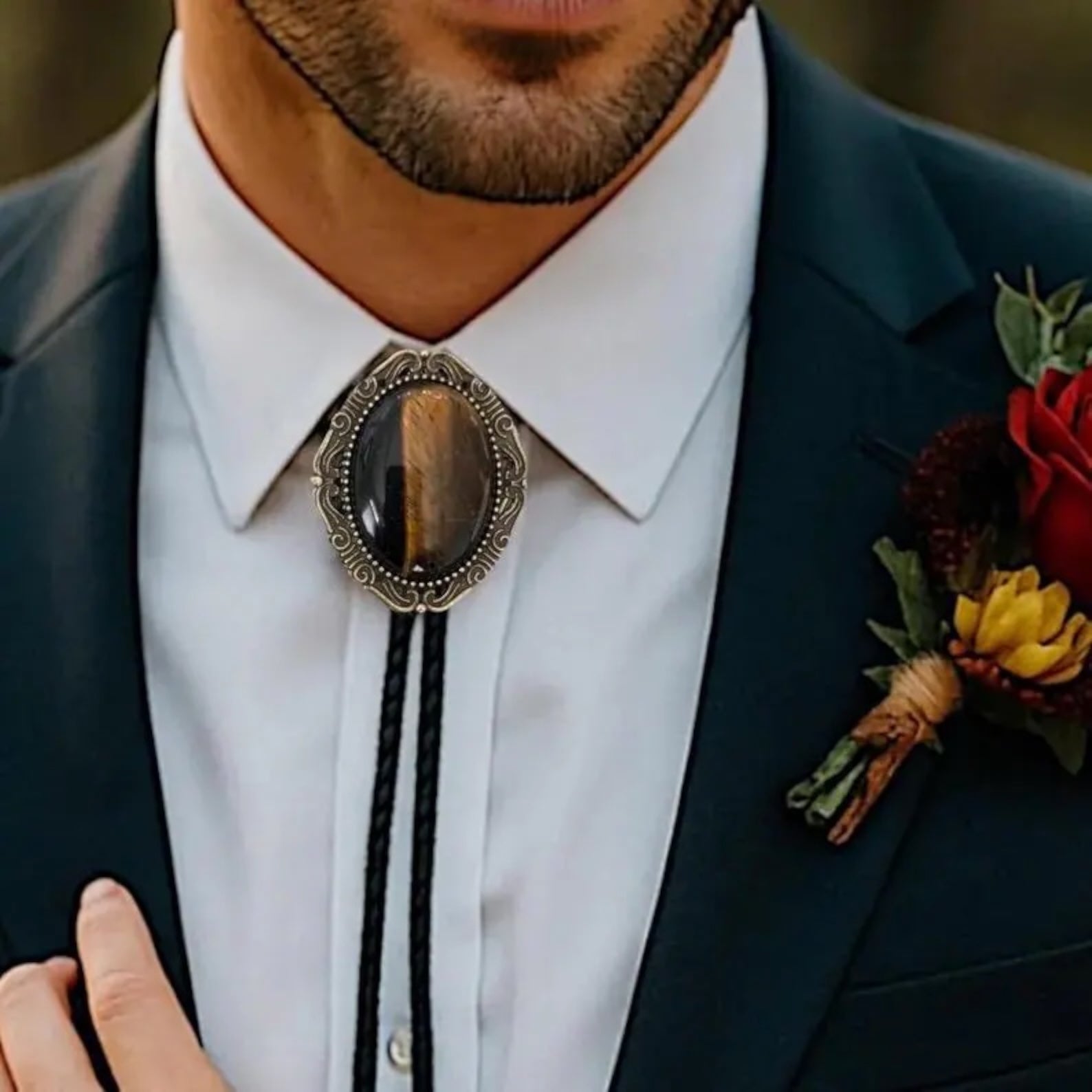 Groomsman wearing a navy suit and tiger’s eye bolo tie with leather cord.