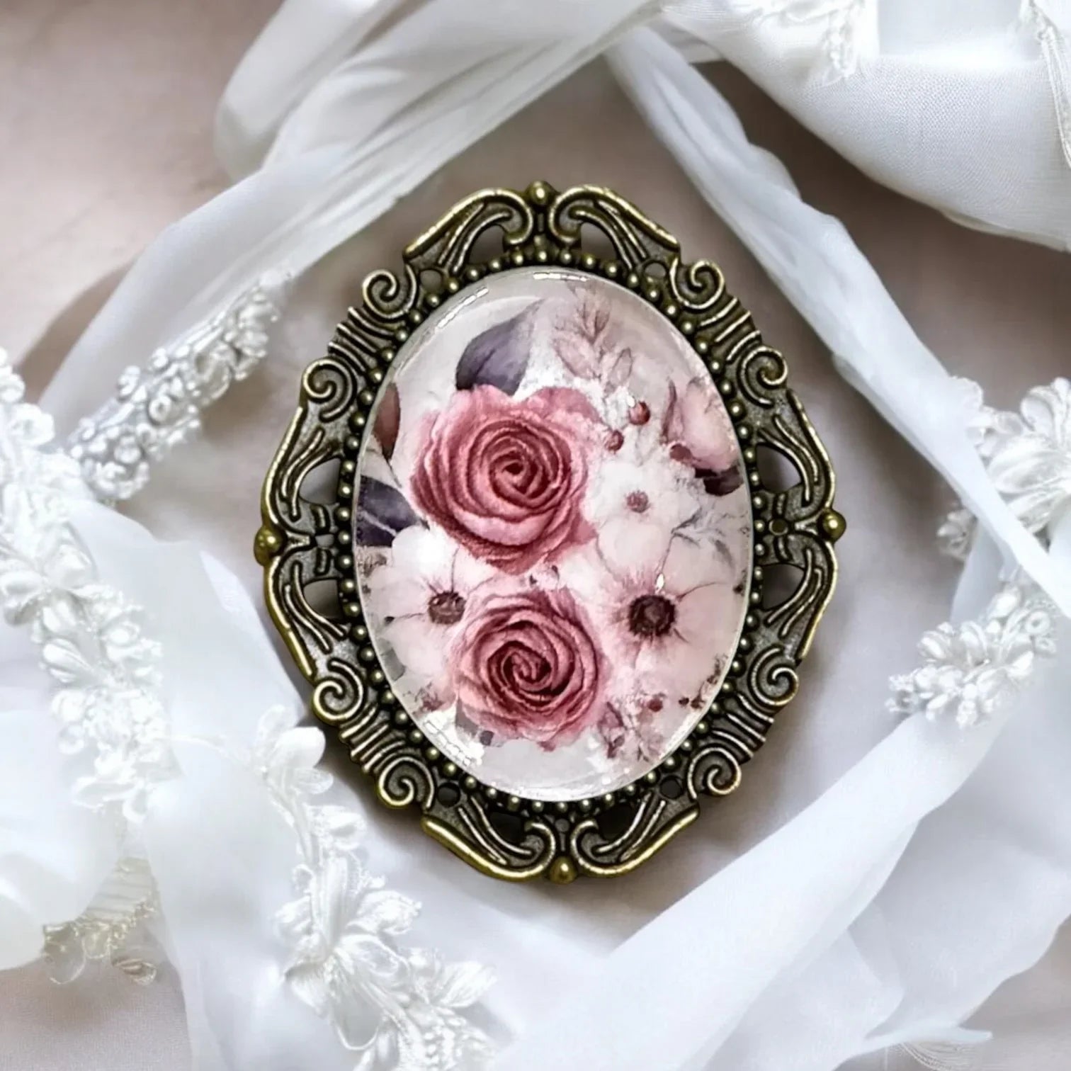 Close up of a vintage oval brooch with pink rose print in an intricate brass frame