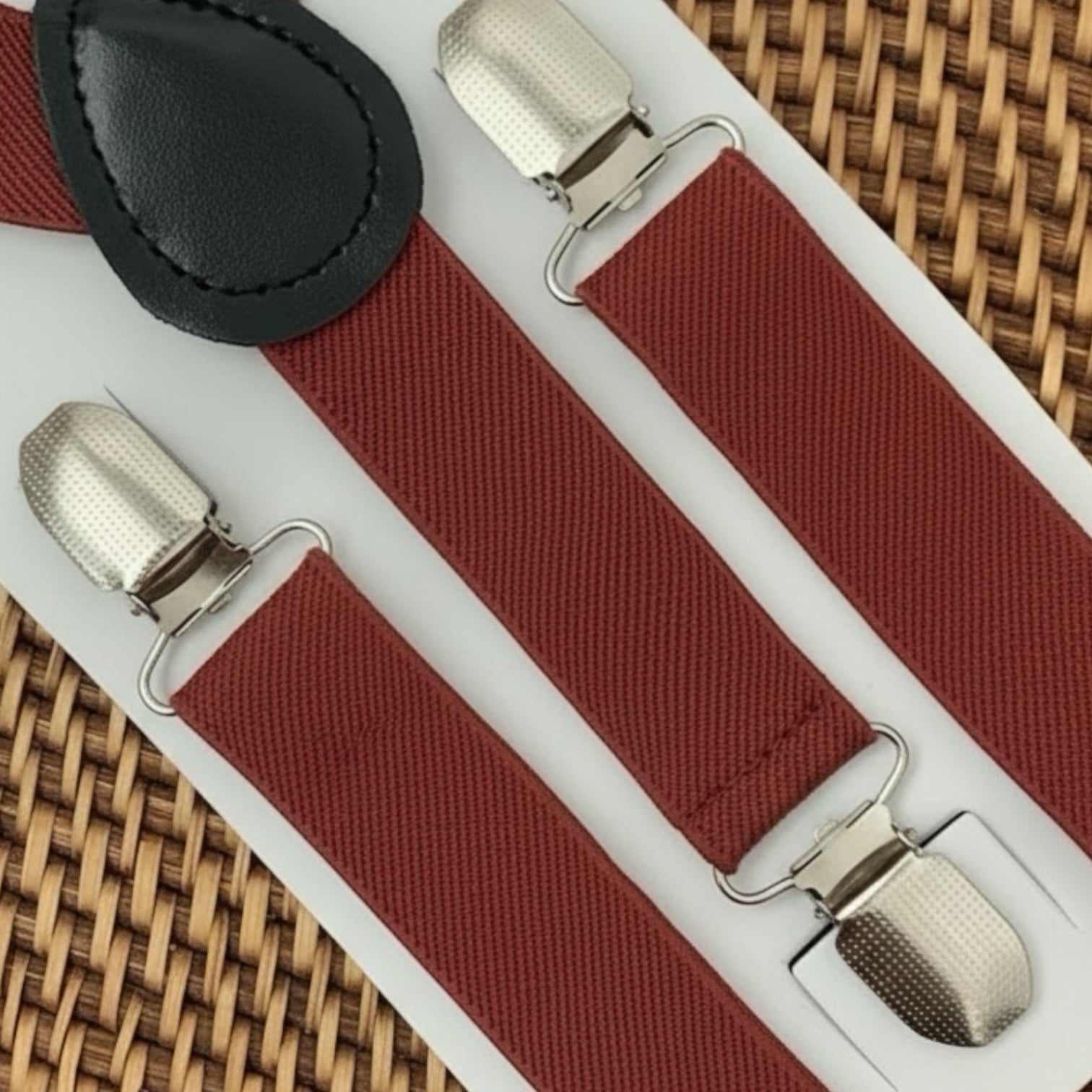 Burnt orange suspenders with silver clips on a white card against a woven background