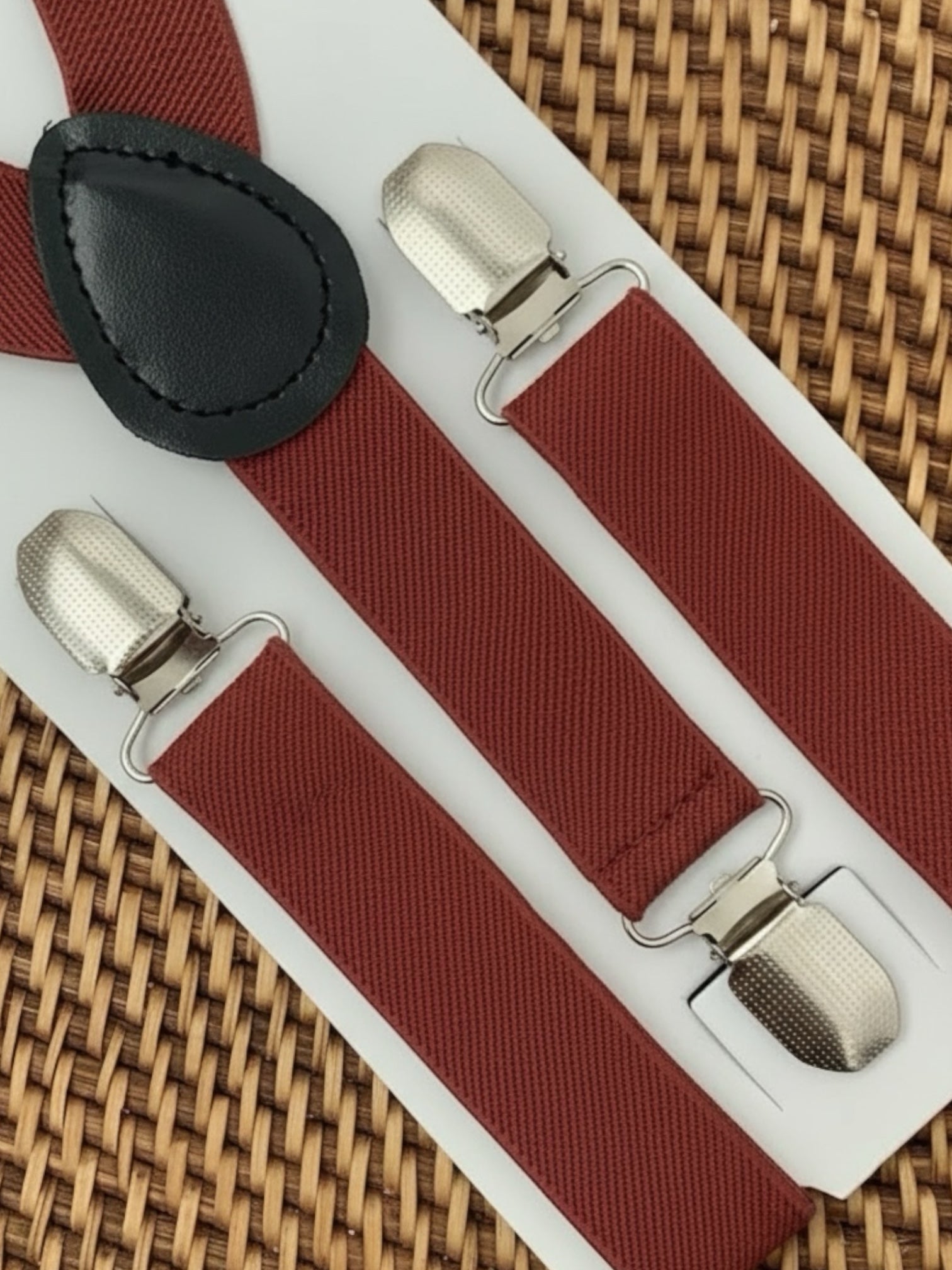 Burnt orange suspenders with silver clips on a white card against a woven background