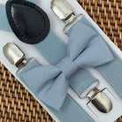 Dusty blue bow tie with silver clips on dusty blue suspenders for groomsmen, ring bearer outfit and wedding on a woven surface