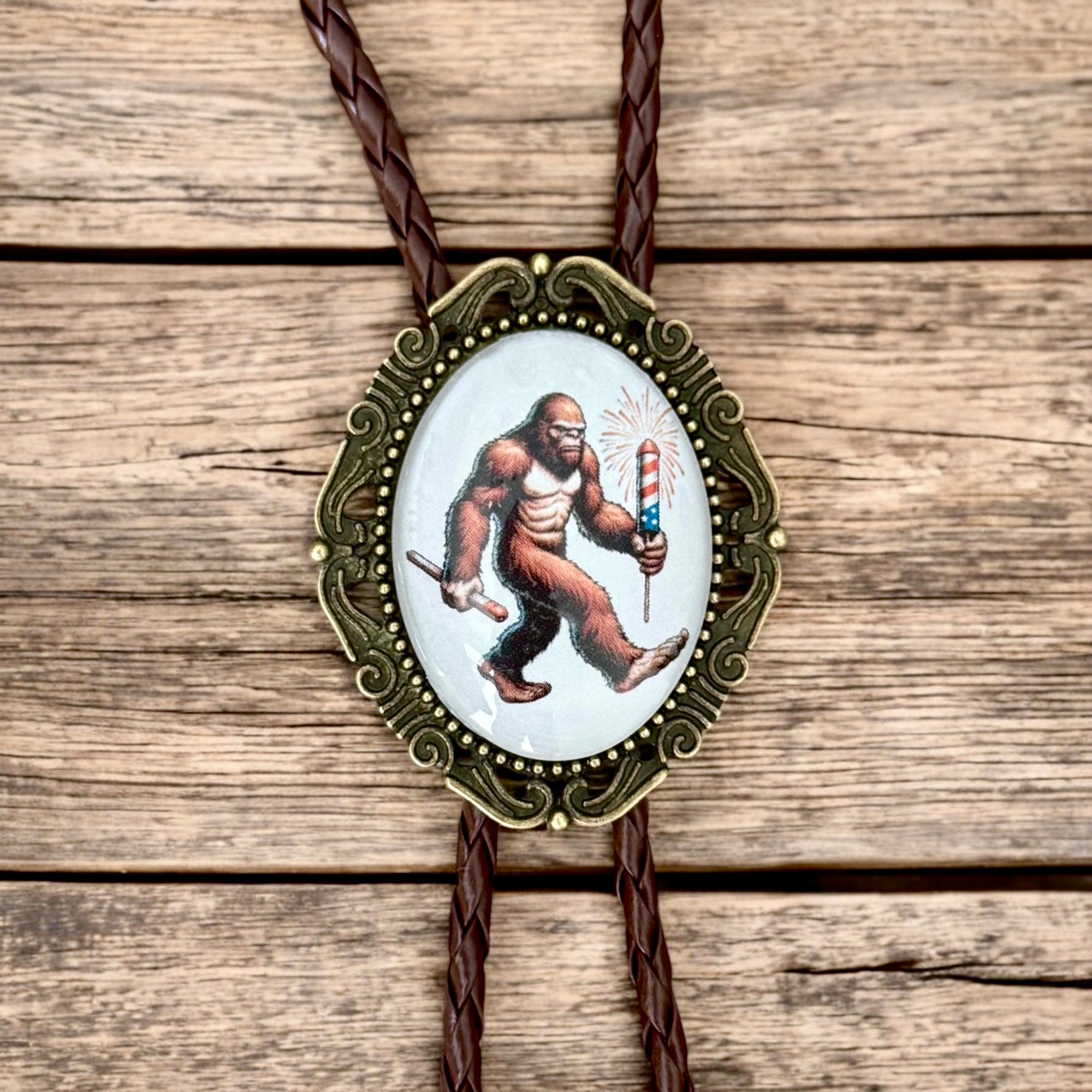 Bolo tie with a design of a big foot holding a firecracker on a wooden surface