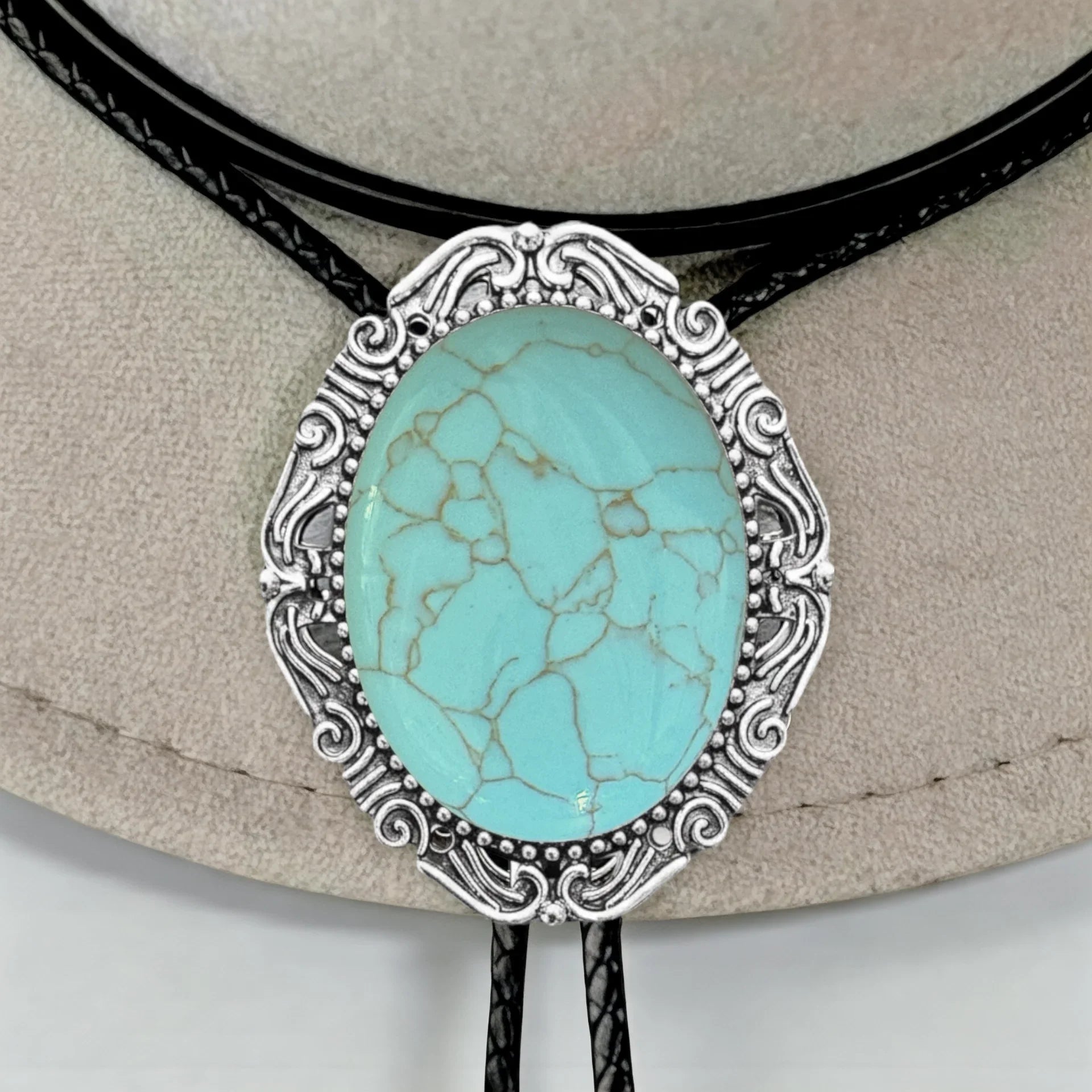 Infographic from The Bold Bow Tie titled Bolo Tie Features. Right: A vintage-style bolo tie with a blue and white cowboy riding a horse illustration inside an ornate bronze filigree frame on a black braided cord. Left: Lines connect the image to three checkmark features: Handmade, 39" Long Cord, and Pendant is 1.5" (L) x 1.25" (W). Bottom text reads Perfect Addition to Your Outfit.