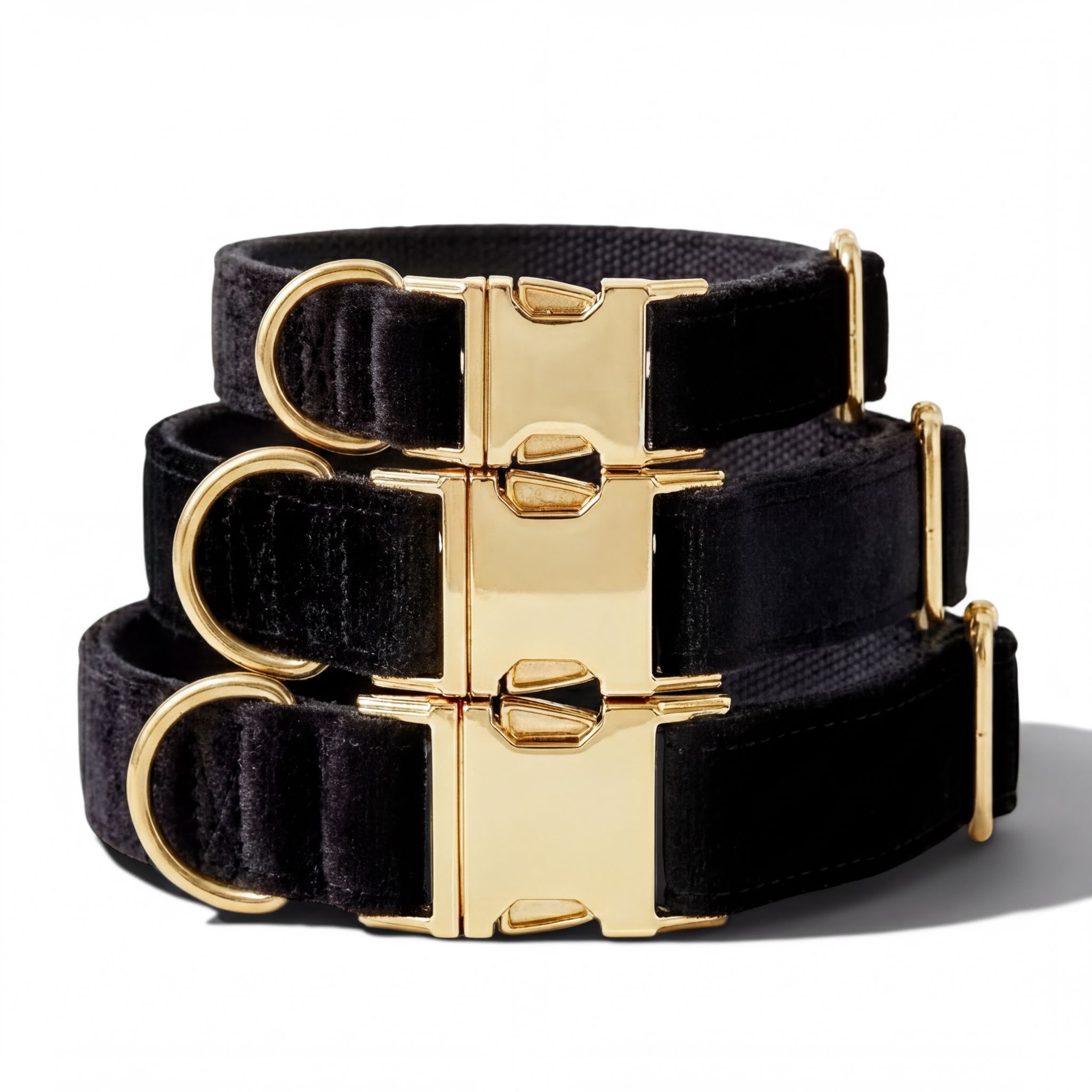 A set of three black velvet dog collars with gold buckles, arranged in a stack.