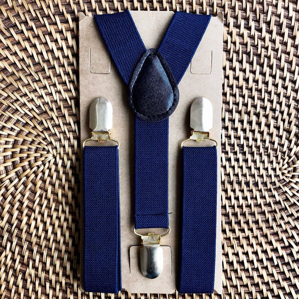 Set of blue suspenders with silver clips on a cardboard backing, placed on a woven surface.