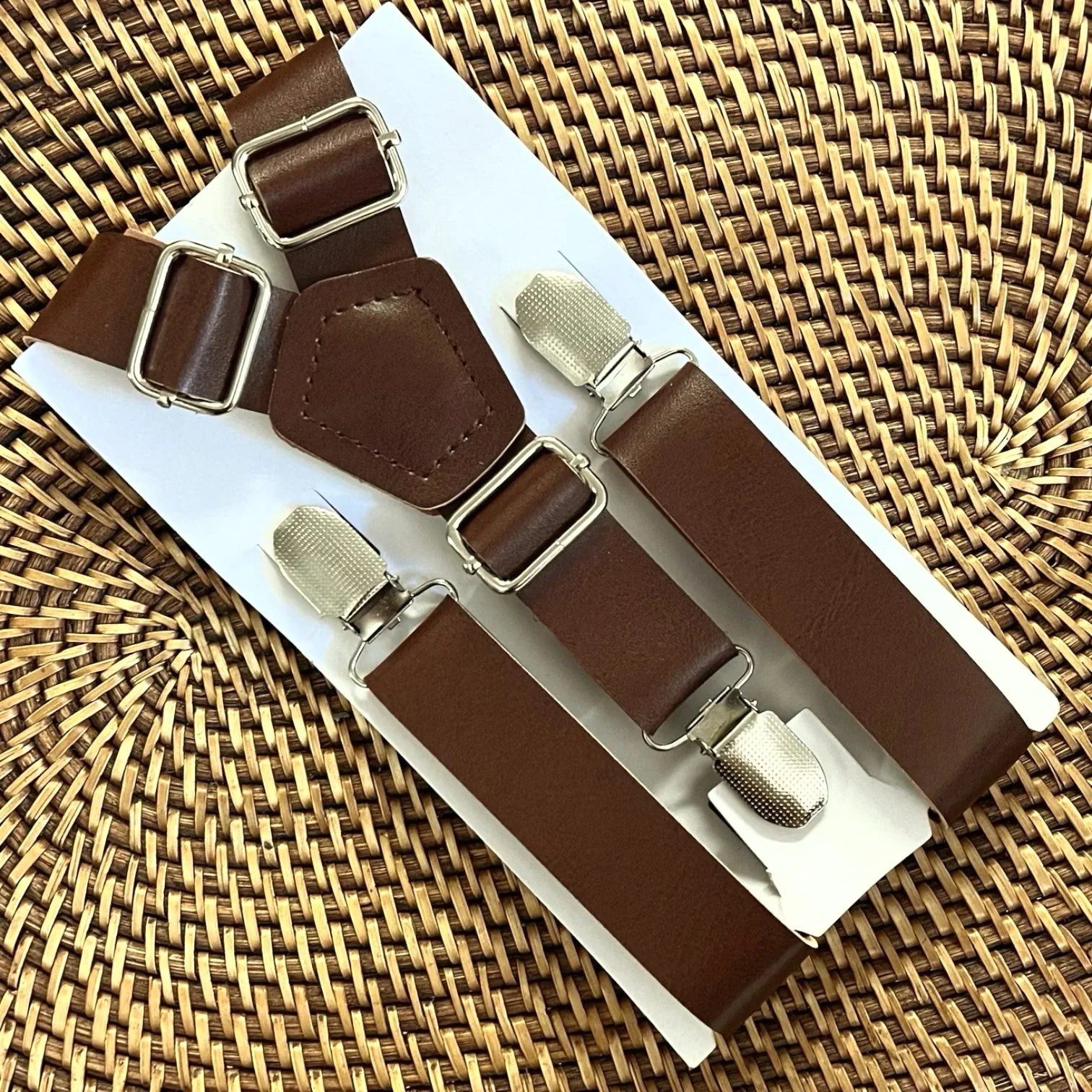Dark brown vegan leather suspenders with silver buckles displayed on packaging against a white background