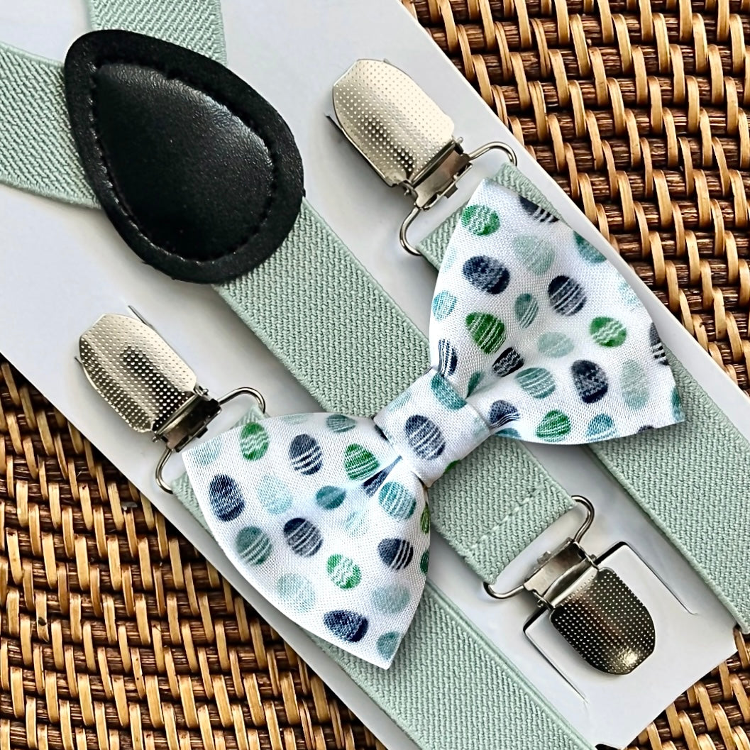 Flat lay of handmade plaid Easter egg bow tie and light green adjustable suspenders set on a brown woven background.