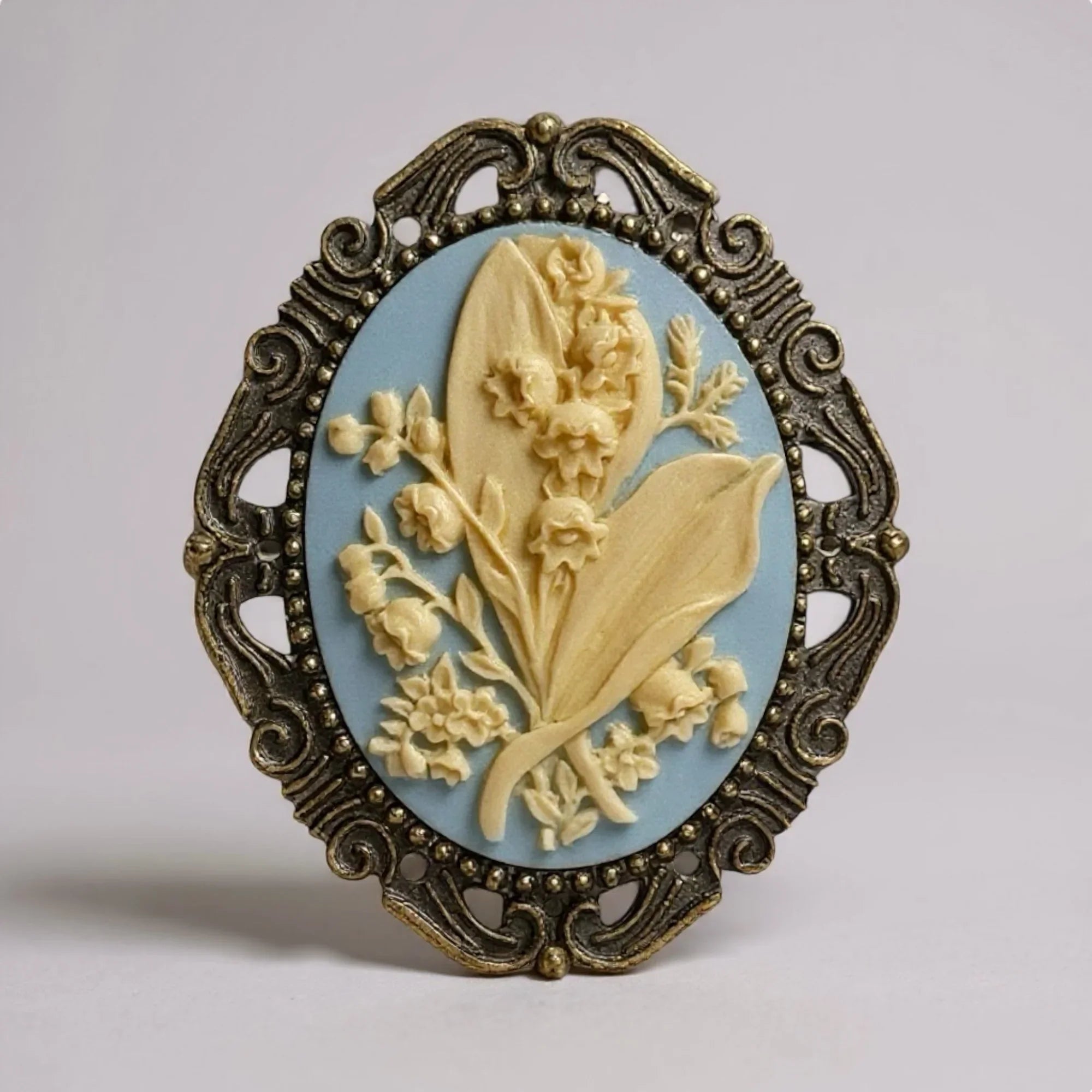 Light blue and ivory floral brooch with floral design and ornate frame on a light gray background