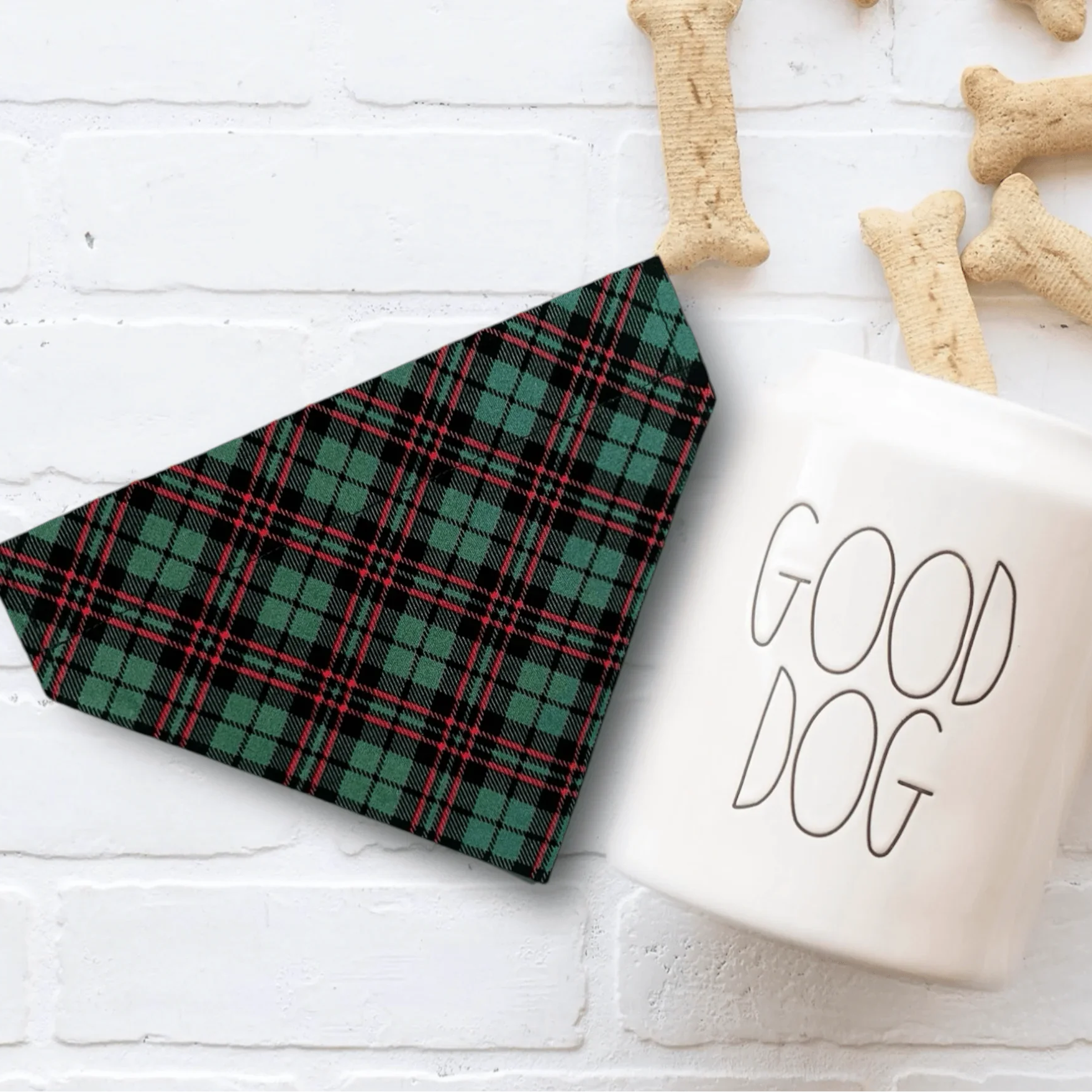 Green plaid Christmas dog bandana displayed on a white surface with bone shaped treats nearby
