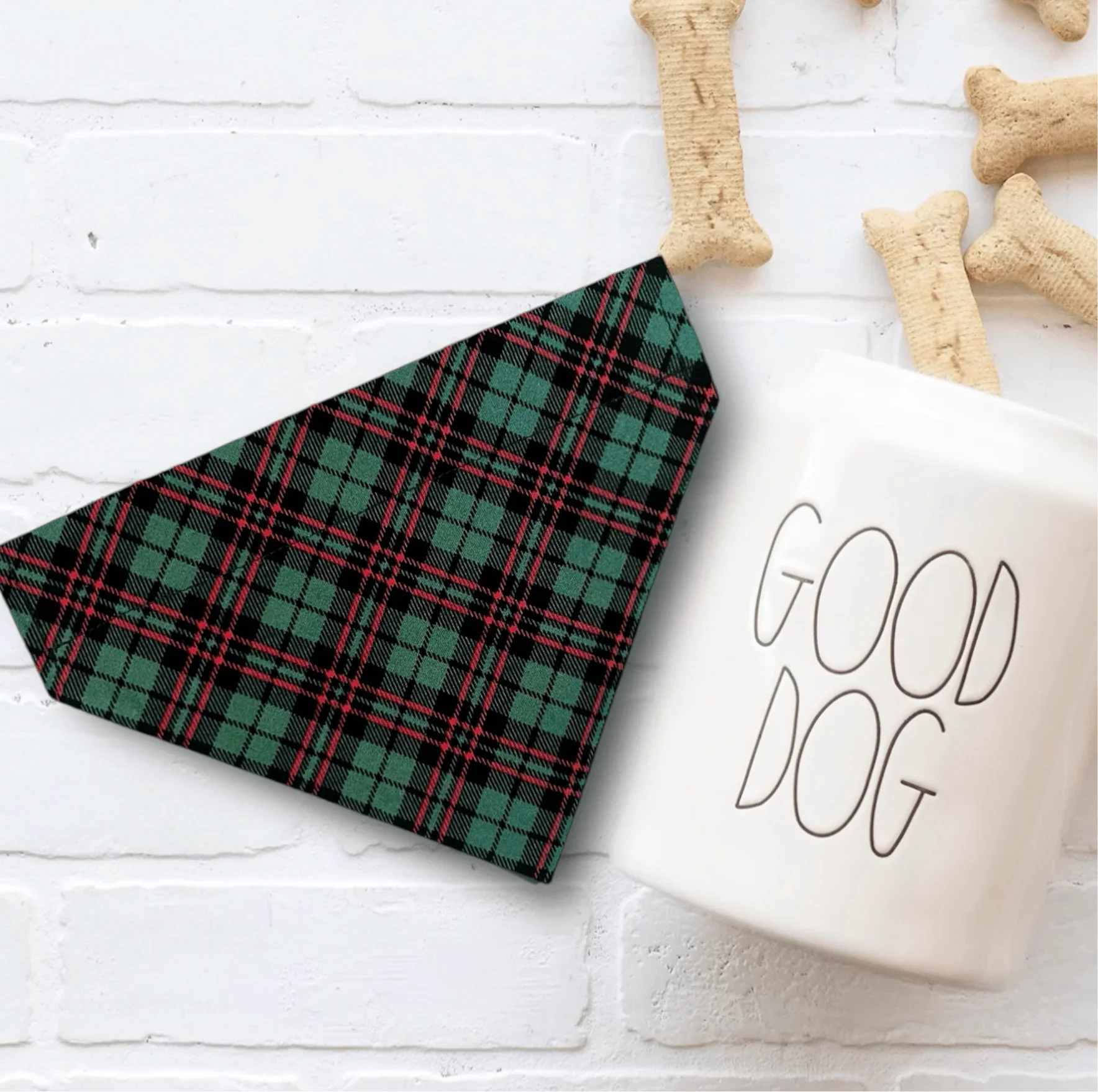 Green plaid Christmas dog bandana displayed on a white surface with bone shaped treats nearby