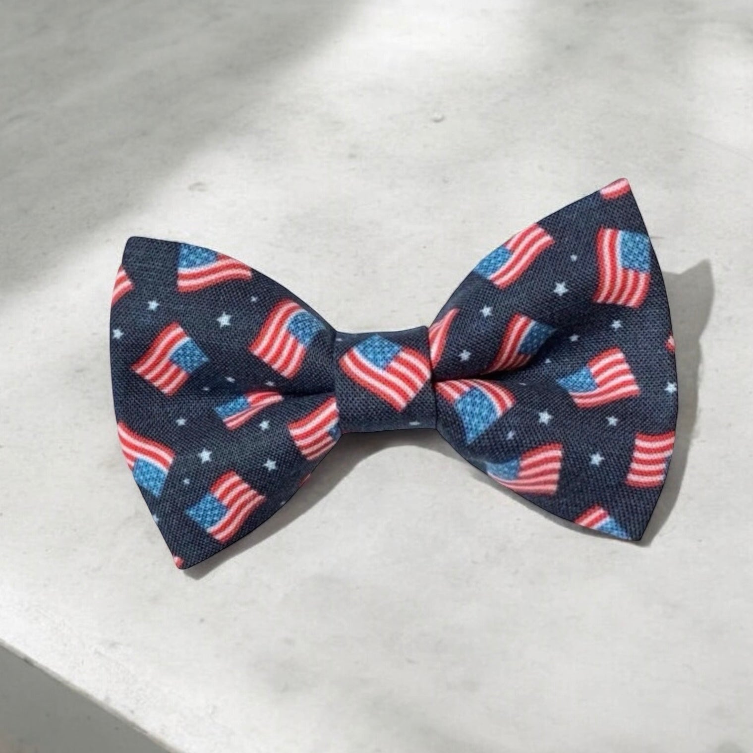 American flag bow tie with small American flags on a navy blue back ground in red white and blue on a concrete table.