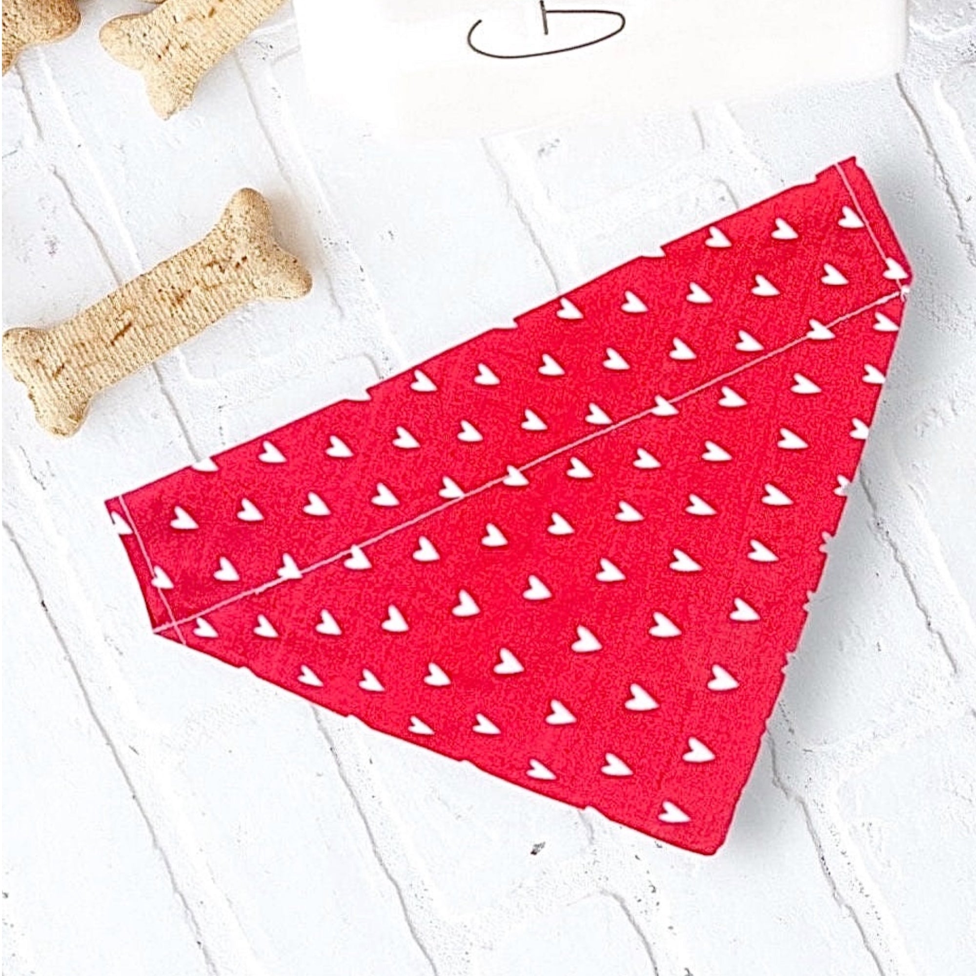 Red Valentines Day dog bandana with white hearts on a light wooden surface