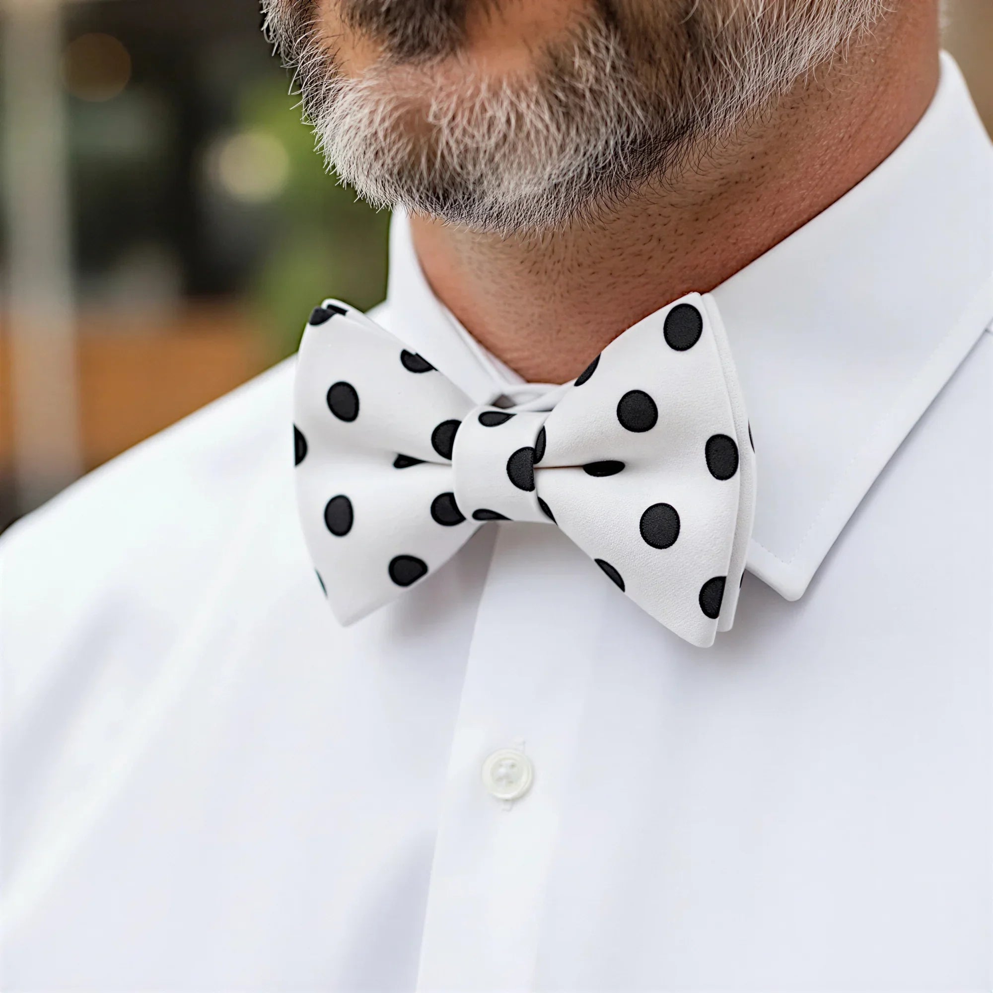 A close-up of a man wearing a white shirt with a black polka dot bow tie.