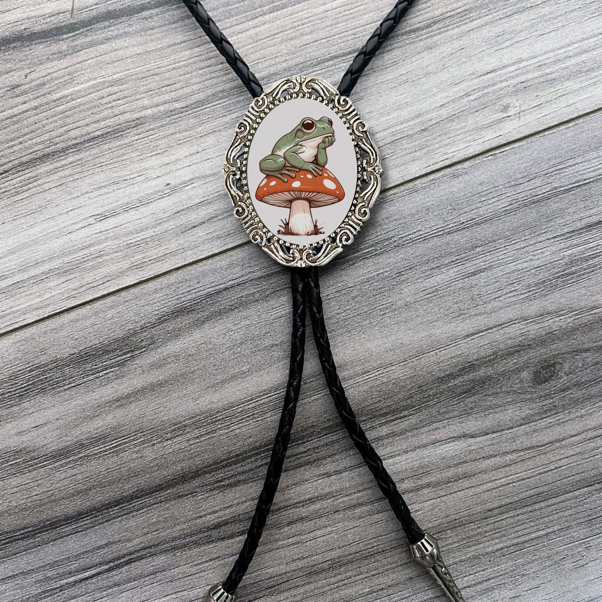 Bolo tie with a frog and mushroom design on a wooden surface