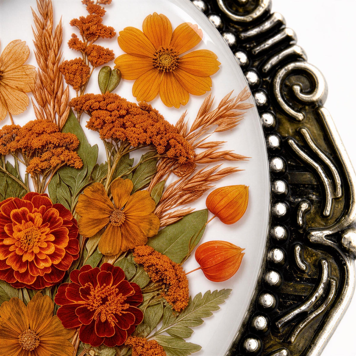 a close-up view of a decorative plate with a variety of orange and red flowers, along with dried flower petals and leaves. The plate has an ornate, decorative metal frame that adds an elegant touch to the overall presentation.