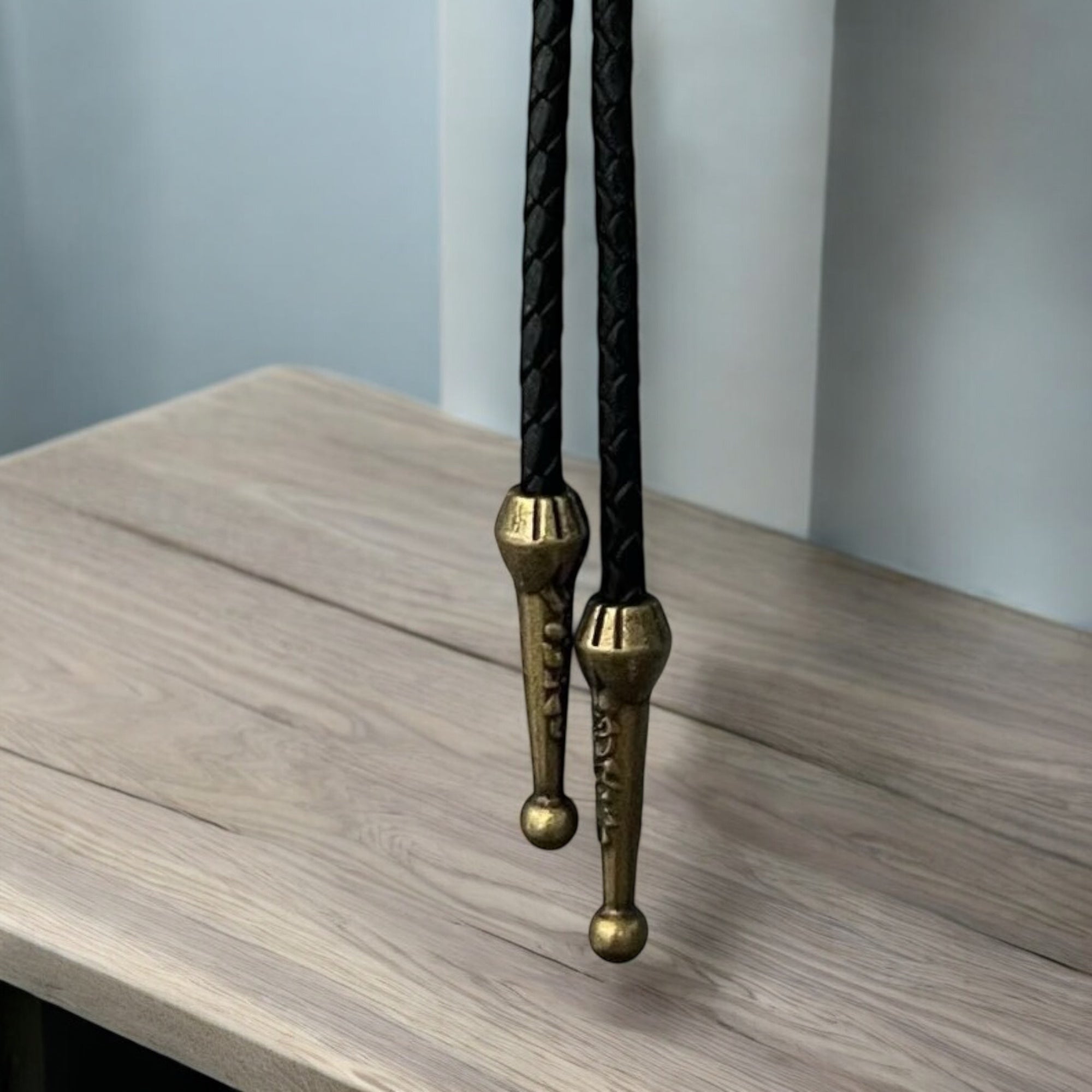 Black leather bolo tie with brass clasp on a wooden surface