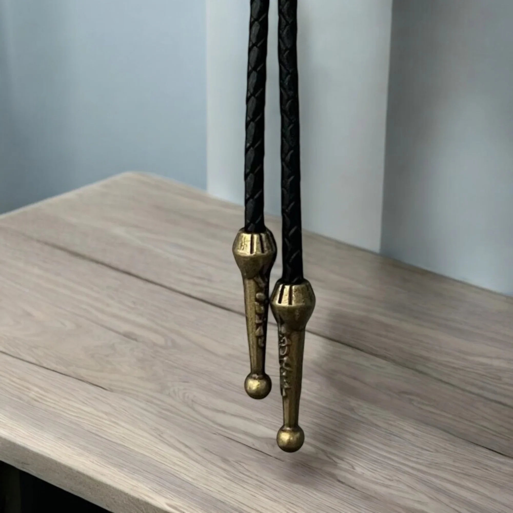 Black leather bolo tie with brass clasp on a wooden surface