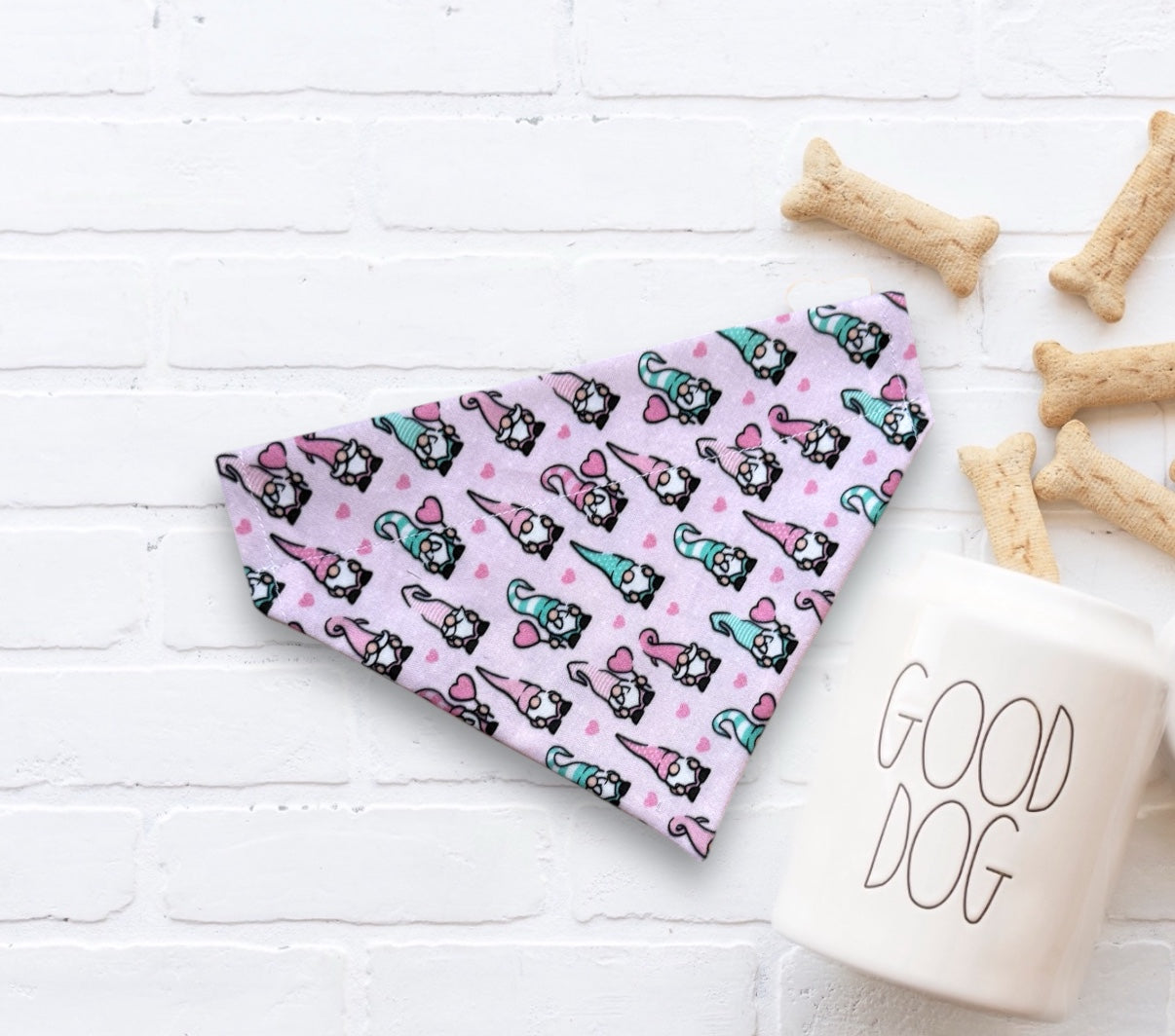 Valentines Day Dog bandana with light pink gnomes on a white surface with dog treats and a 'Good Dog' mug.