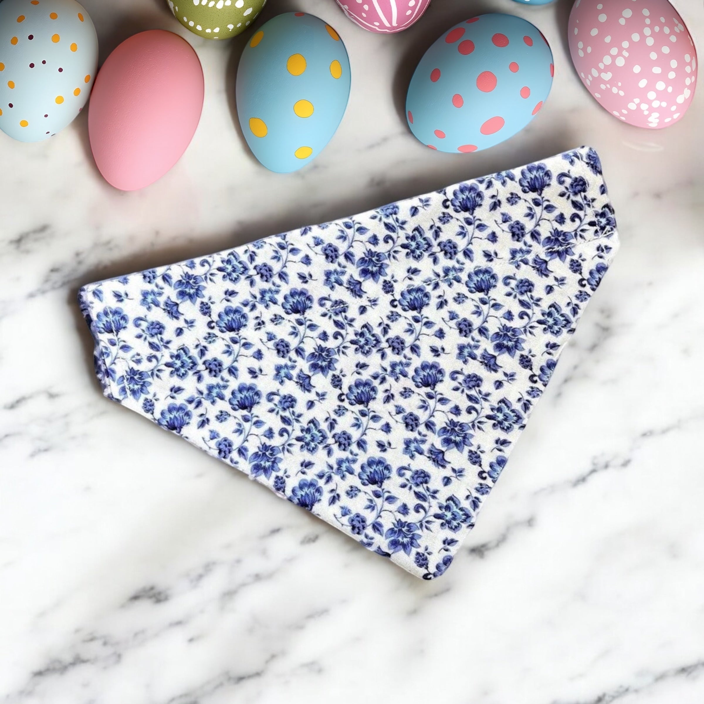 Floral dog bandana for Easter on a marble surface with colorful Easter eggs in the background