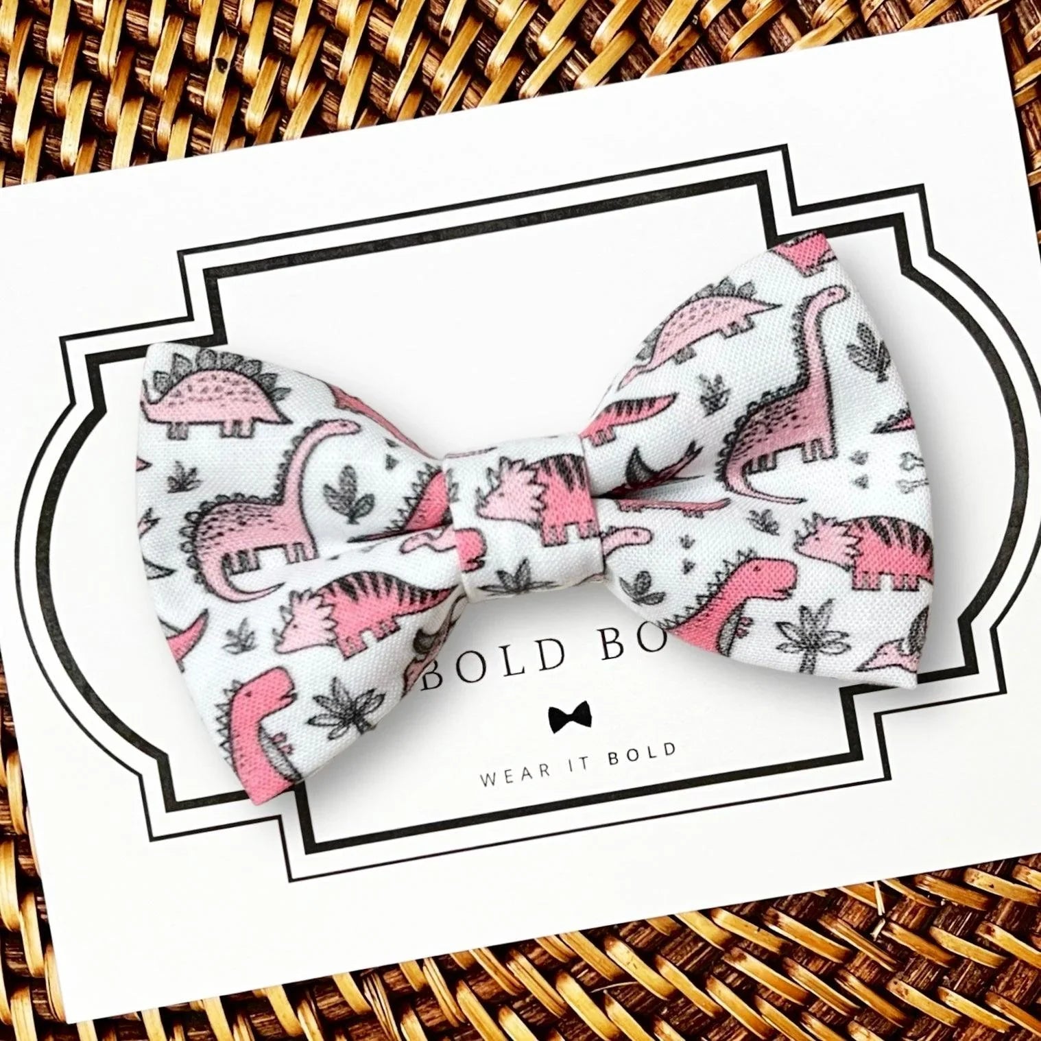 Pink and black dog dinosaur bow tie on a white card with 'The Bold Bow Tie, Wear It Bold' branding.