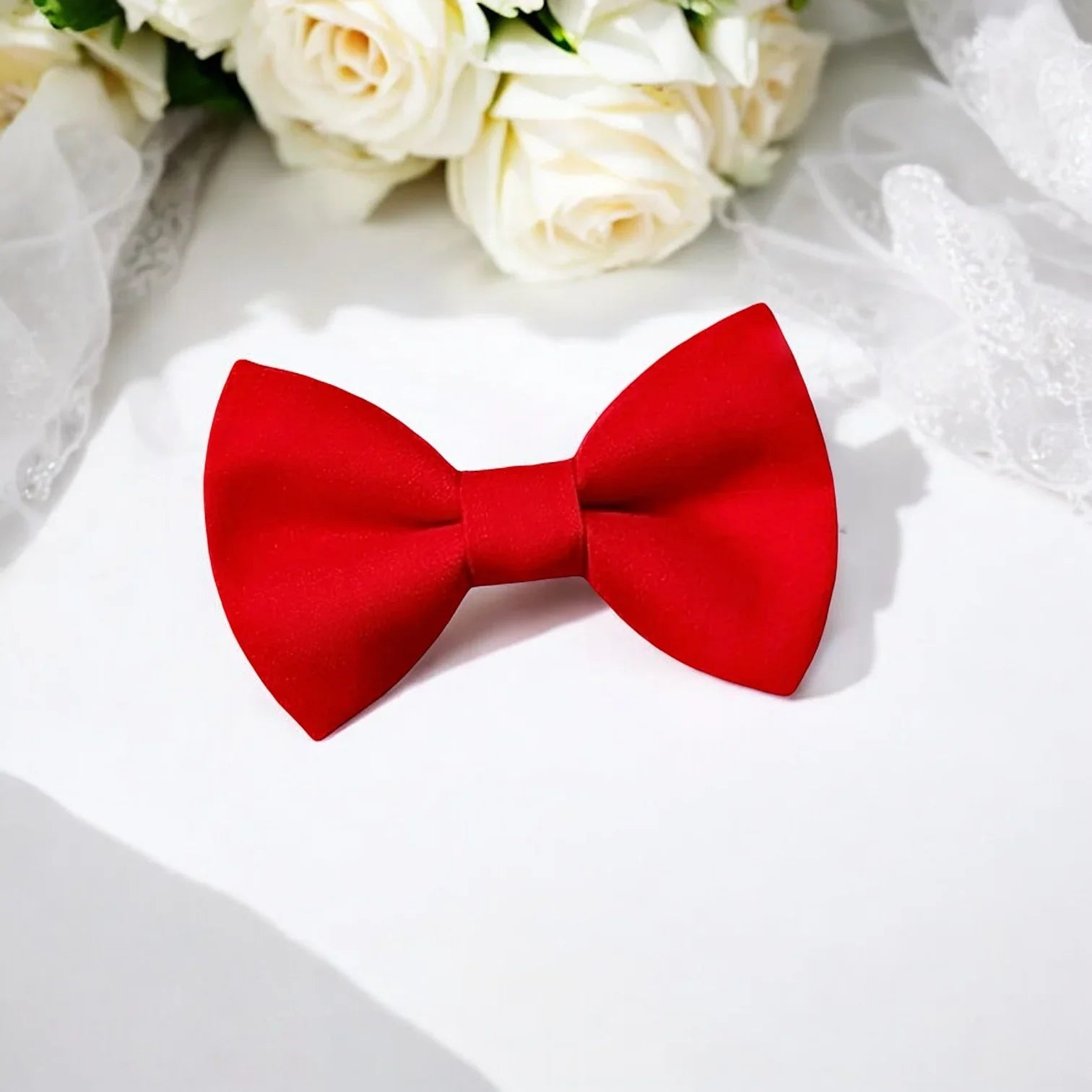 Red cotton bow tie on a white surface with white roses in the background